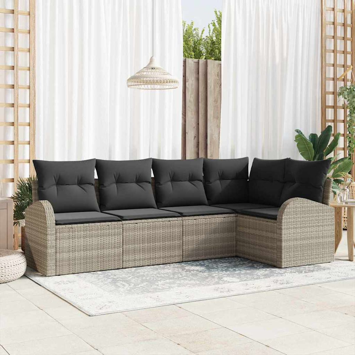 Ein Ecksofa im Freien mit grauen Kissen. Es steht auf einem Teppich, mit Vorhängen und Grün im Hintergrund.