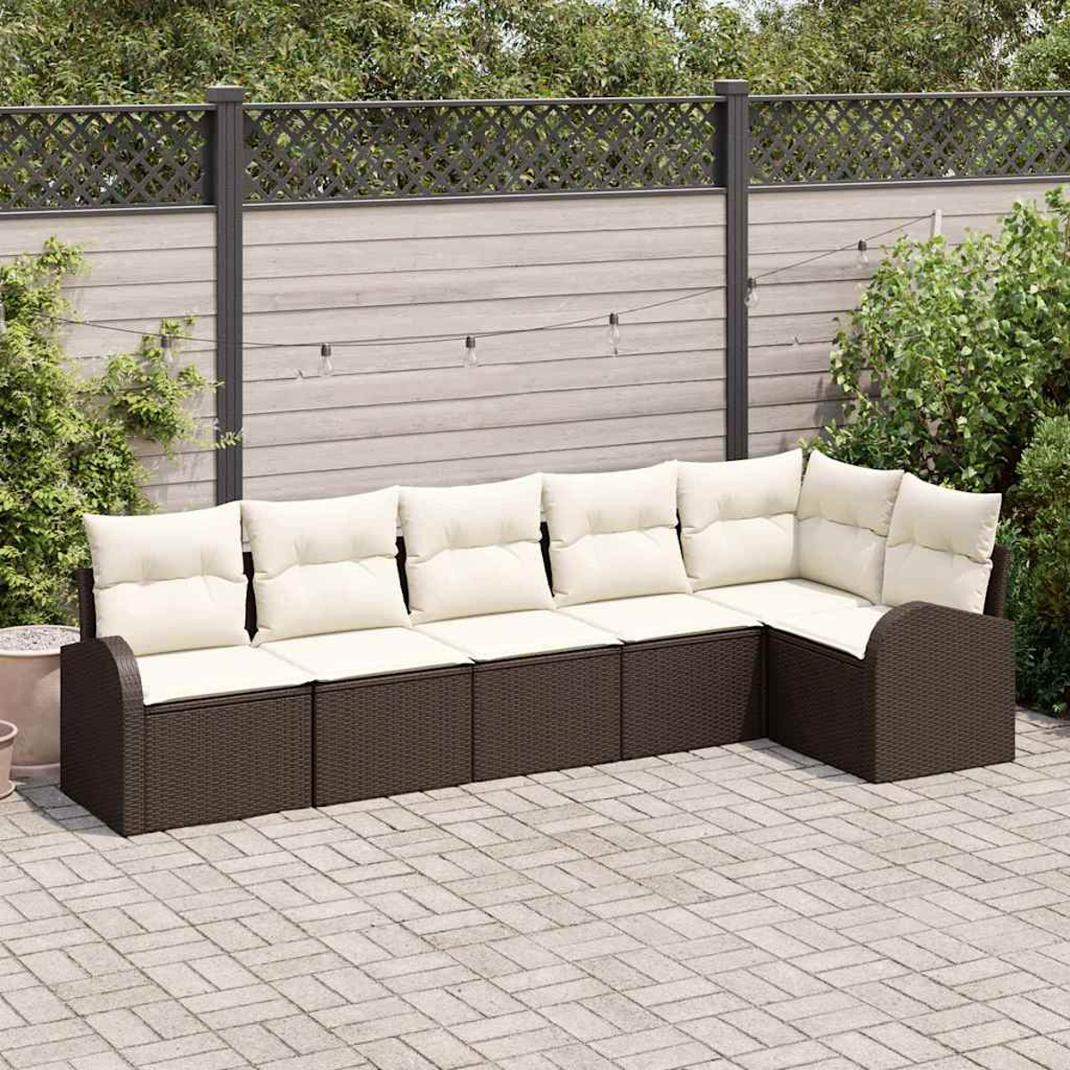 Ein braunes Ecksofa aus Korbgeflecht mit cremefarbenen Kissen steht auf einer Ziegelterrasse. Ein Zaun und Grünzeug im Hintergrund.
