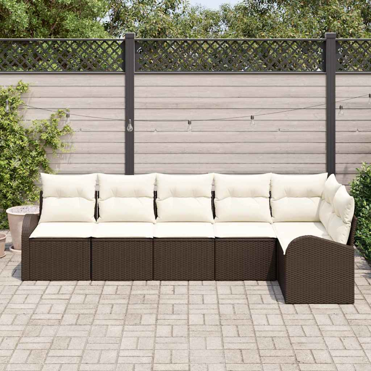 Outdoor-Ecksofa mit cremefarbenen Kissen auf einer Ziegelterrasse. Hintergrund sind Zaun, Laub und Lichterketten.