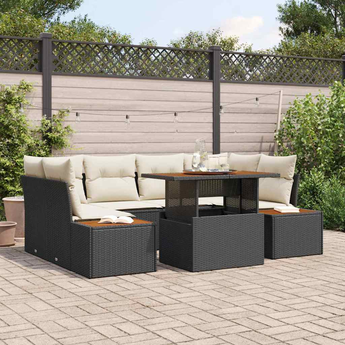 Garten-Lounge-Set mit schwarzer gewebter Möblierung, beigen Kissen und einem Holztisch. Im Hintergrund ein Zaun und Grün.