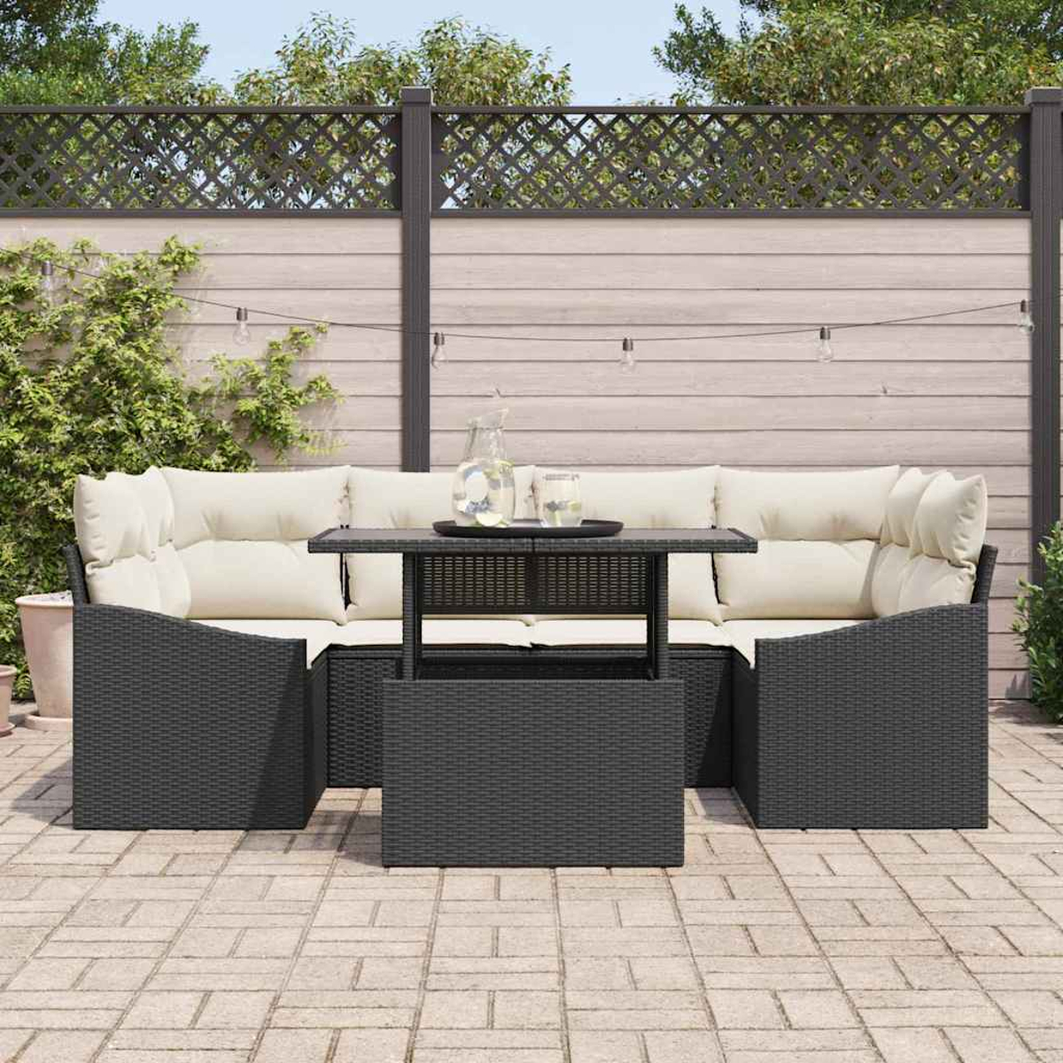 Garten-Terrassenset mit schwarzen Korbmöbeln und cremefarbenen Kissen, Tisch mit Getränken, Lichterketten und Holzzaun.