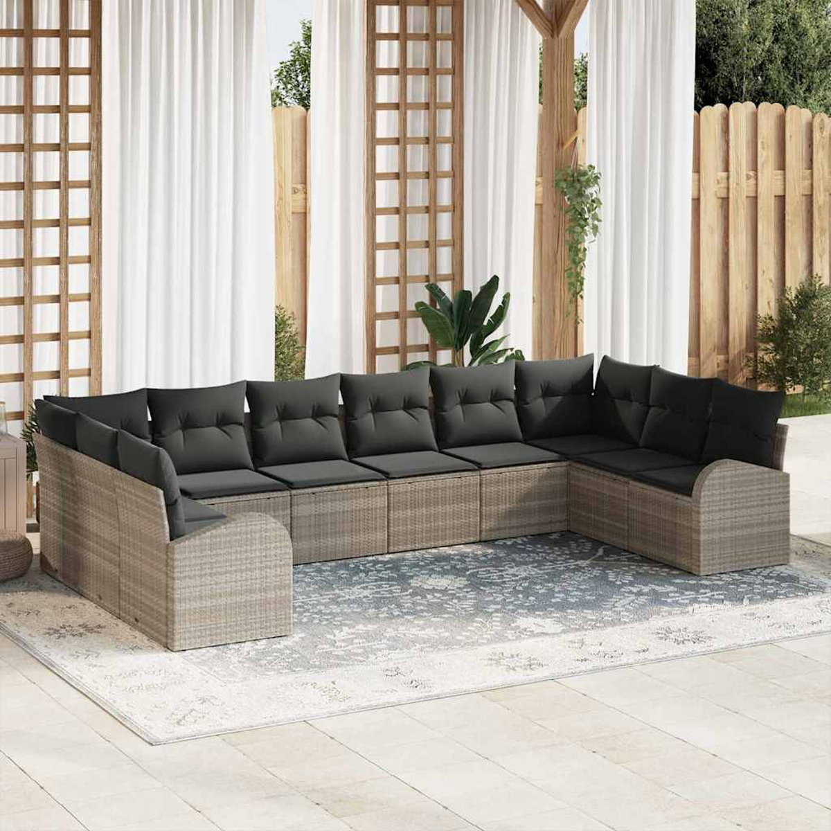 Ein Ecksofa mit grauen Kissen im Freien steht auf einem Teppich. Weiße Vorhänge und ein Holzzaun sind im Hintergrund.