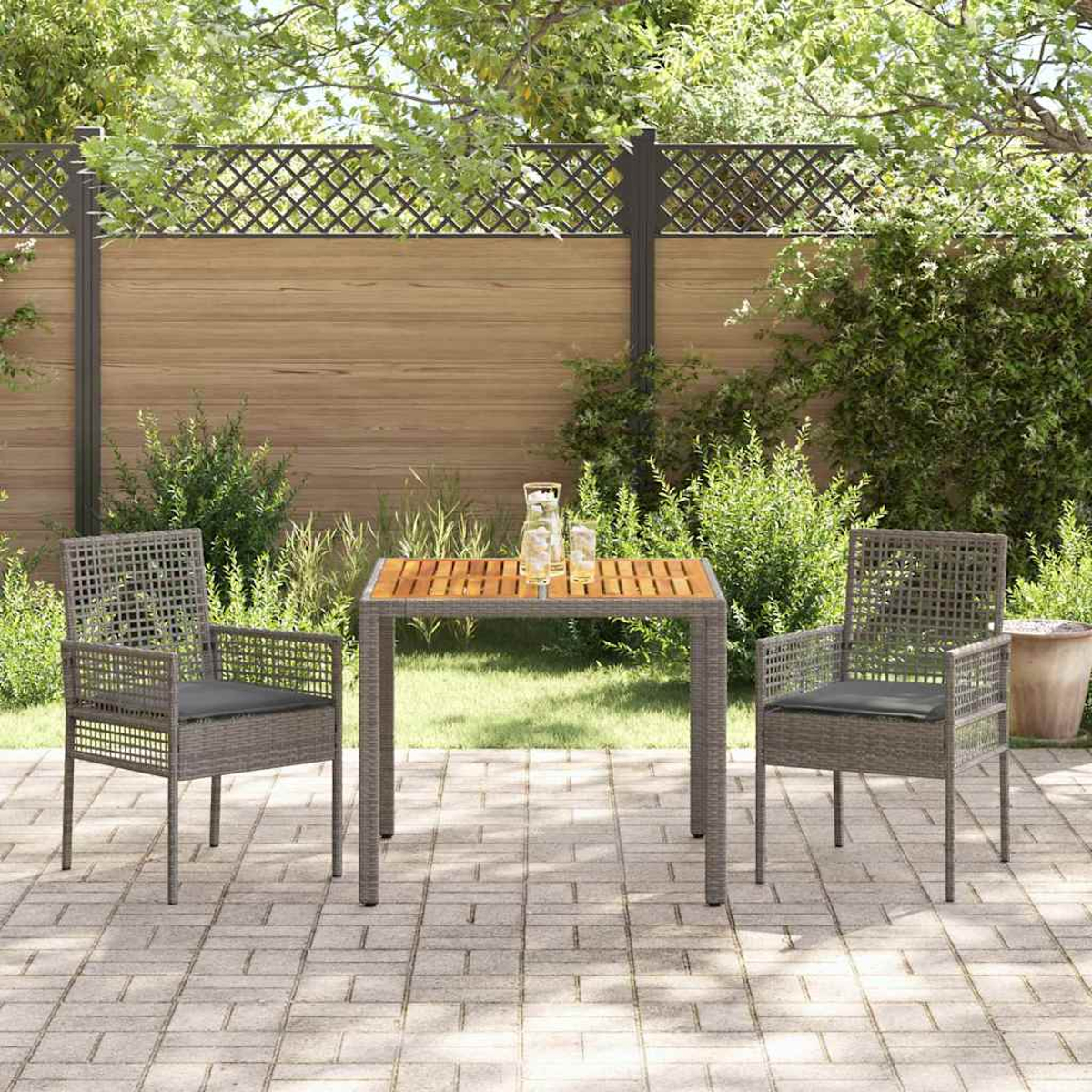 Outdoor-Patio-Set mit Tisch und zwei Stühlen auf einer Ziegelterrasse, umgeben von Grün und einem Holzzaun.