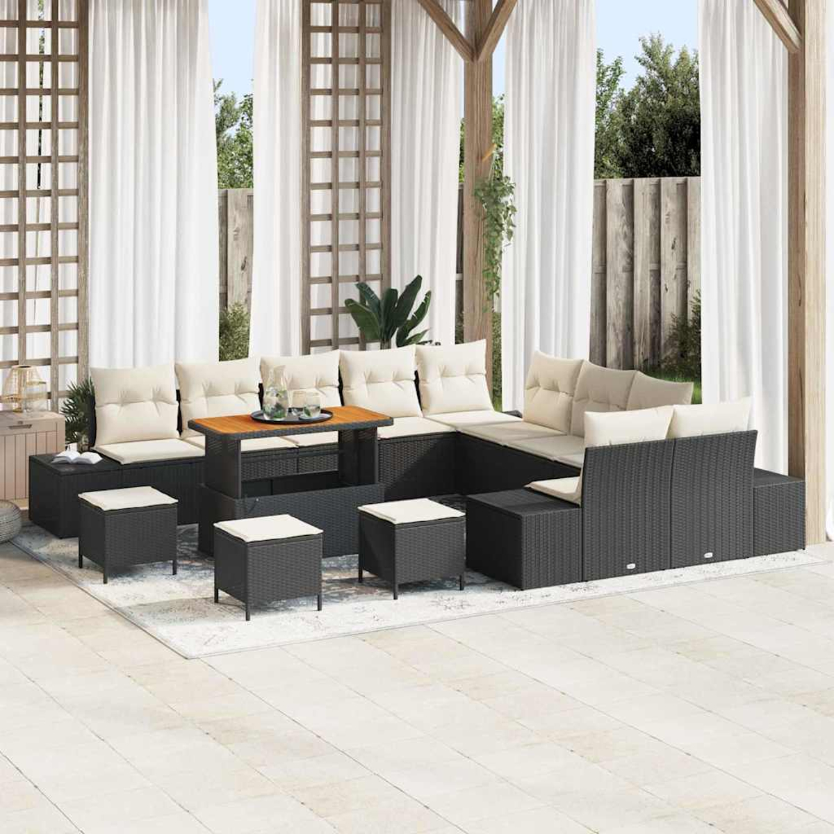 Outdoor-Sitzgruppe mit schwarzen Korbmöbeln, beigen Kissen und einem Holztisch. Weiße Vorhänge, ein Teppich und eine hellfarbige Terrasse.