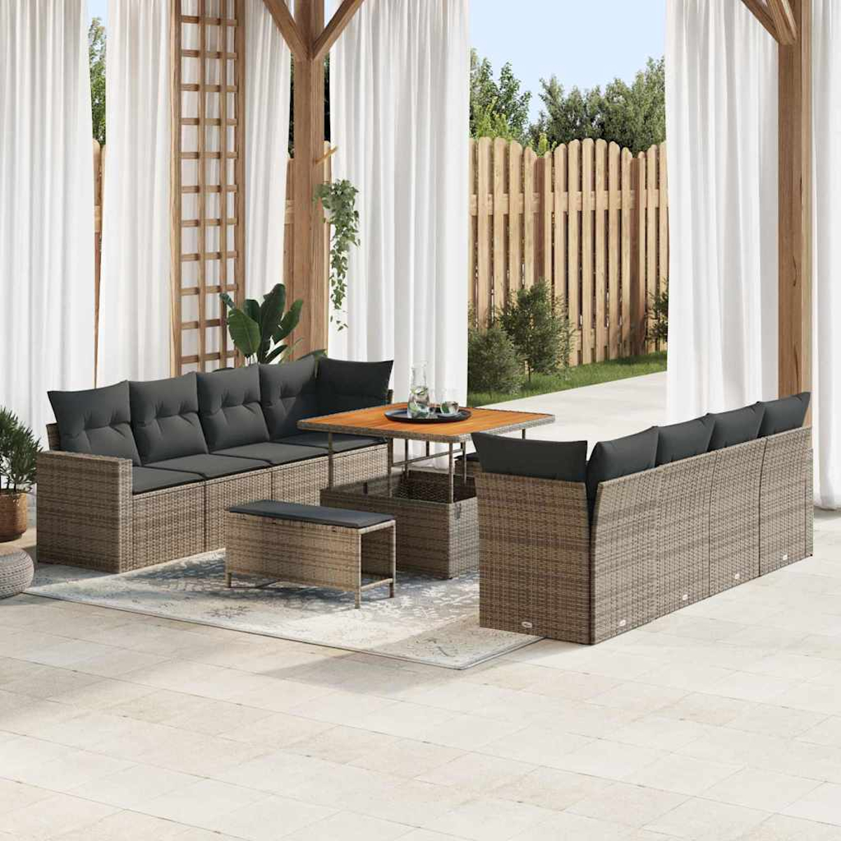 Gartenmöbel-Set aus Rattan mit grauen Kissen auf einer Terrasse. Enthält Sofa, Tisch, Bank und Holzzaun im Hintergrund.