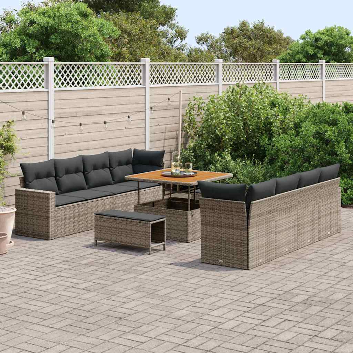 Garten-Sitzgruppe auf einer Terrasse. Enthält ein Sofa, eine Doppelsitz, einen Tisch und eine Ottomane. Ein weißer Zaun und Grünzeug sind im Hintergrund.