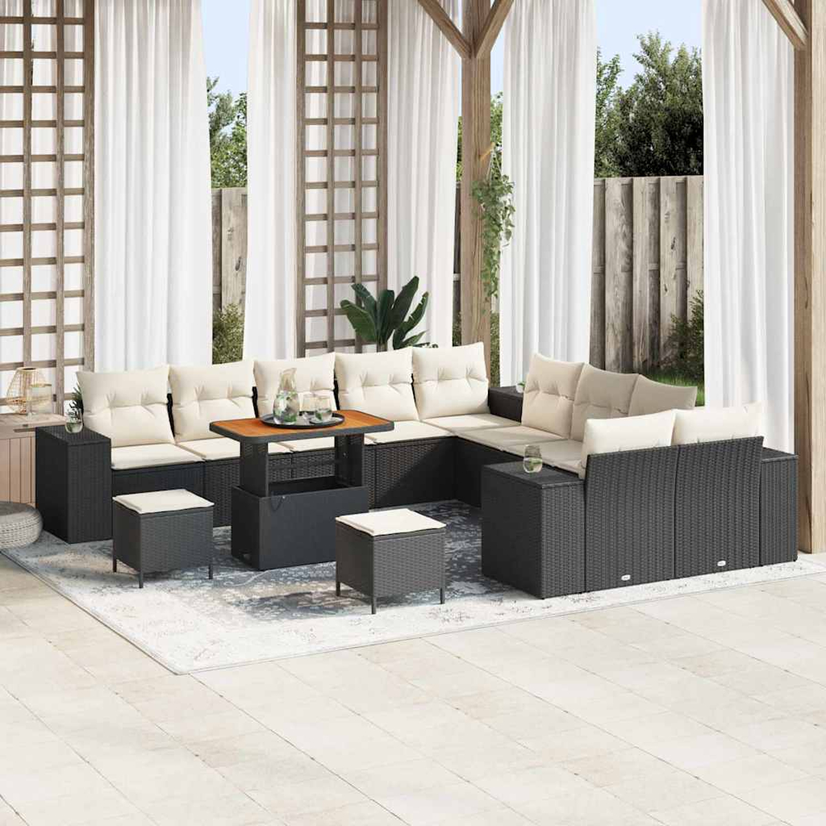 Terrassenset mit schwarzer Korbmöbel, cremefarbenen Kissen und einem Holztisch. Weiße Vorhänge und ein hellfarbiger Teppich.