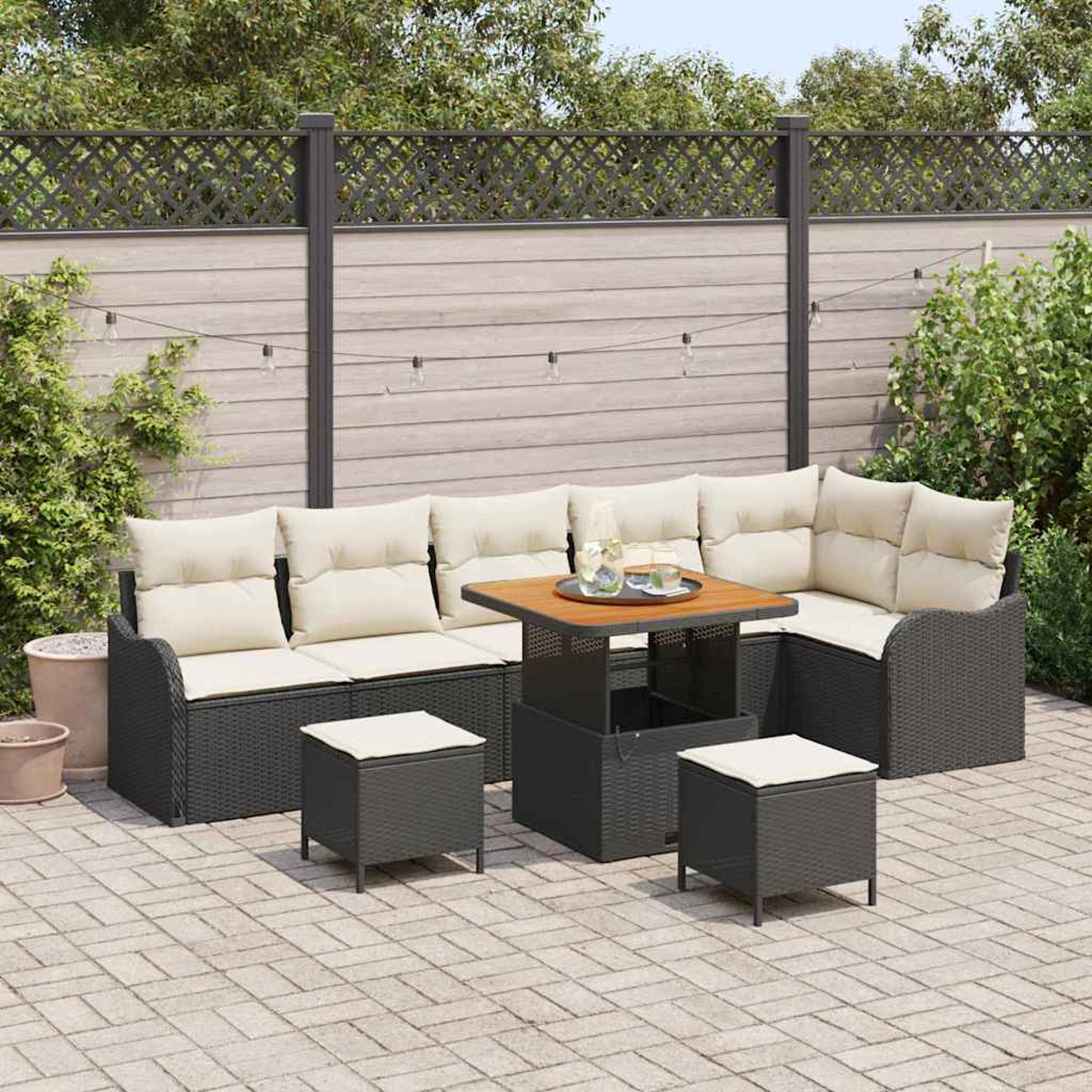 Garten-Sitzgruppe mit cremefarbenen Kissen, einem Tisch und zwei Hockern auf einer Backstein-Terrasse, mit Zaun und Laub im Hintergrund.