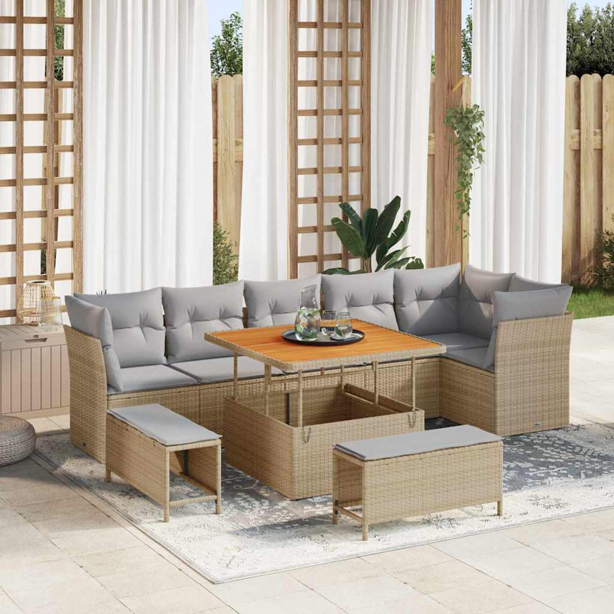 Outdoor-Korbmöbel-Set mit grauen Kissen, einem Holztisch mit Getränken und einem neutralen Teppich auf einer Terrasse mit weißen Vorhängen.