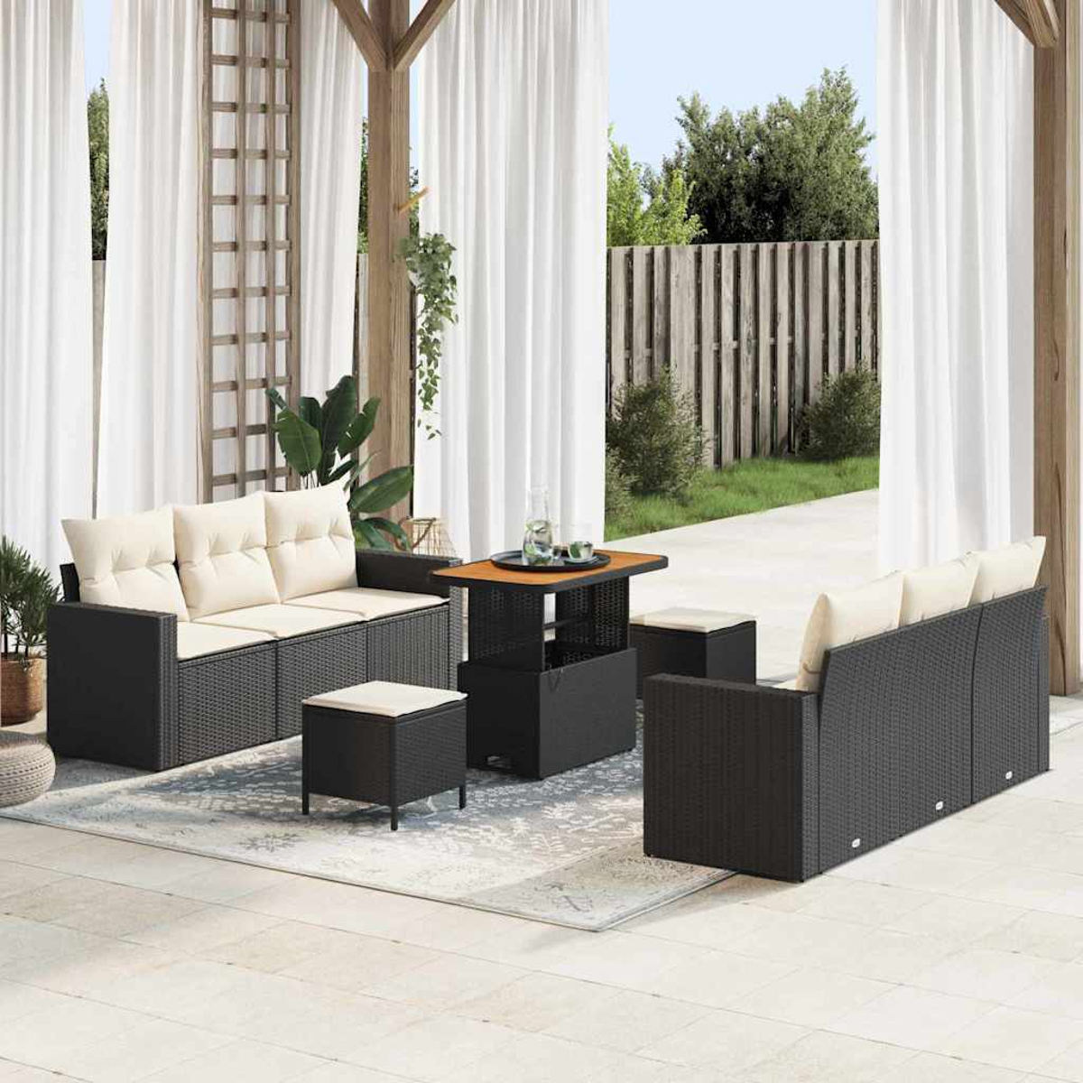 Terrassen-Set mit schwarzen Korbsesseln, Ottomanen und einem Tisch. Weiße Vorhänge und ein Holzzaun sind im Hintergrund.