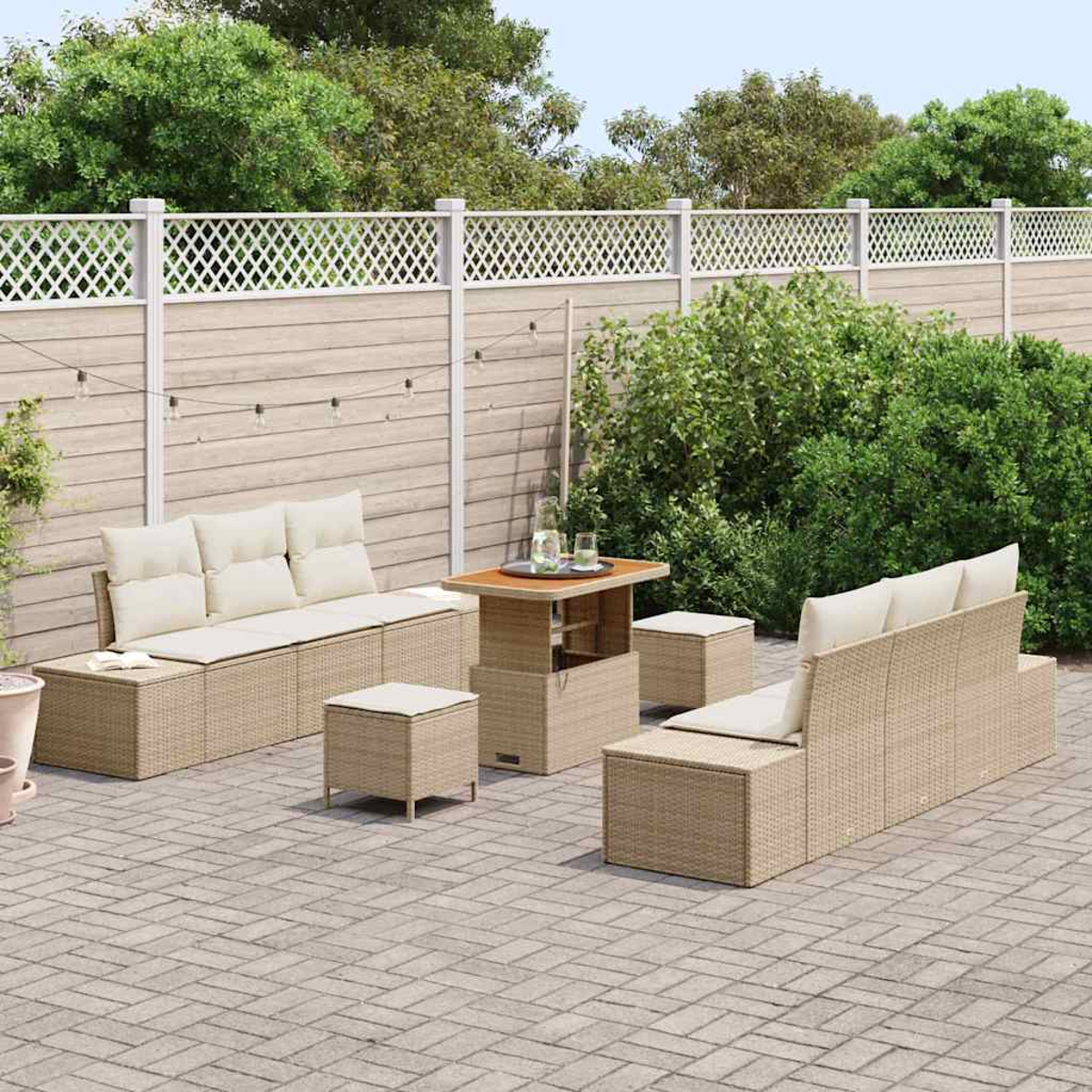 Garten-Set mit beigen Korbmöbeln, darunter ein Sofa, Tisch und Hocker, auf einer Ziegelsteinterrasse, mit weißem Zaun und Grün.