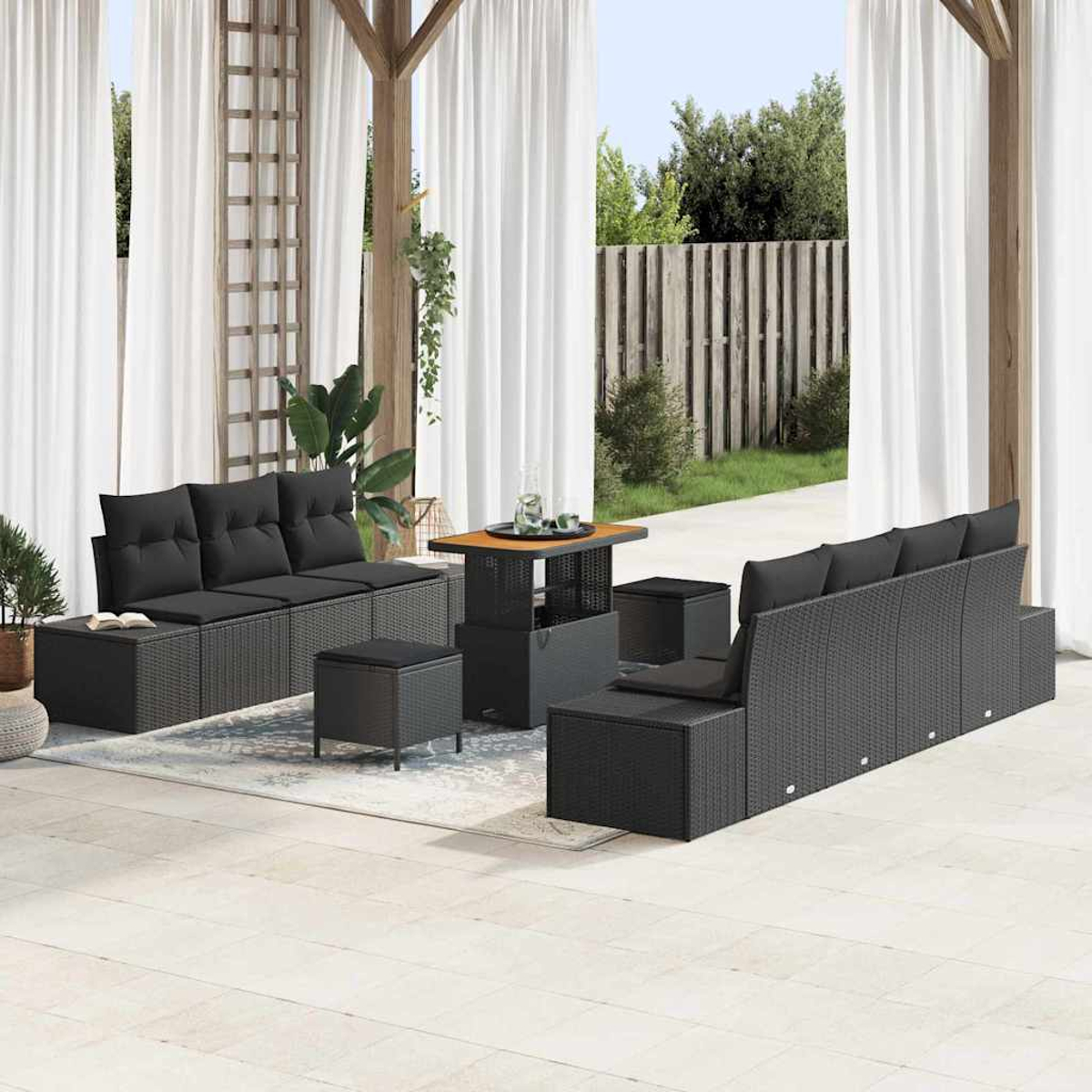 Gartenmöbel-Set. Schwarze Korbsessel, Ottomanen und ein Tisch. Weiße Vorhänge, Pflanzen und eine Holzkonstruktion im Hintergrund.