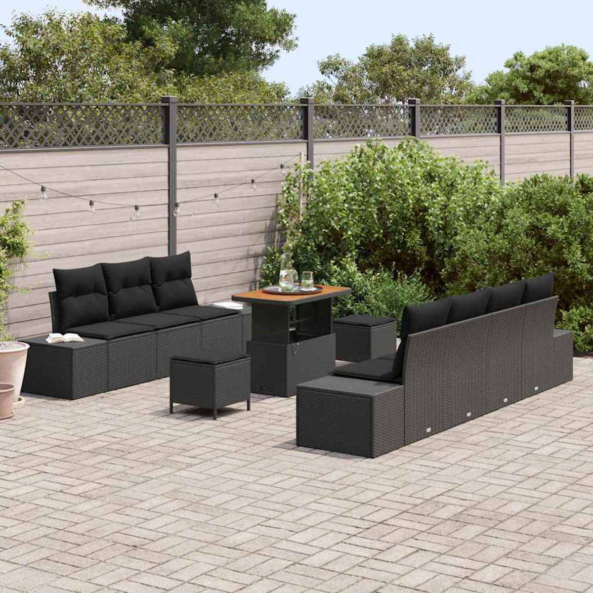 Gartenmöbel-Set. Enthält Sofa, Ottomanen und Tisch. Auf Ziegelpflaster mit Zaun und Grün im Hintergrund.