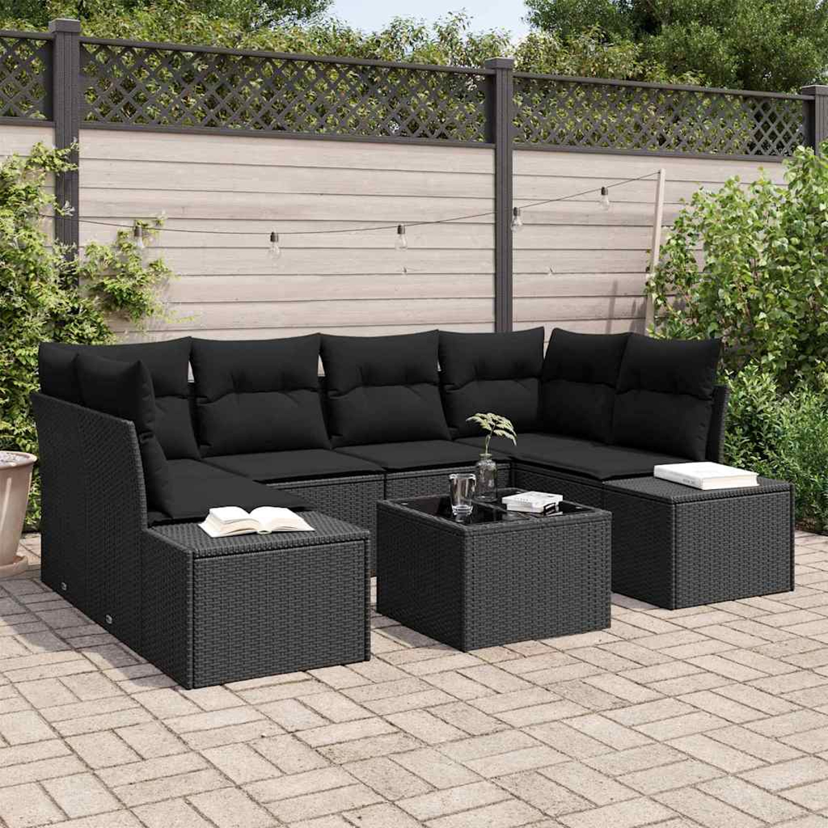Juego de muebles de mimbre negro para exteriores con cojines, mesa de cristal y libro. En un patio pavimentado, fondo de valla de madera y vegetación.
