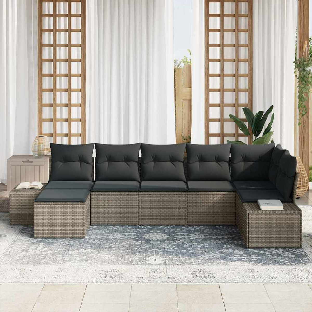 Ein Ecksofa im Freien mit dunklen Kissen steht auf einem gemusterten Teppich. Dahinter sind Vorhänge und Holzgitter, die eine Terrasse bilden.