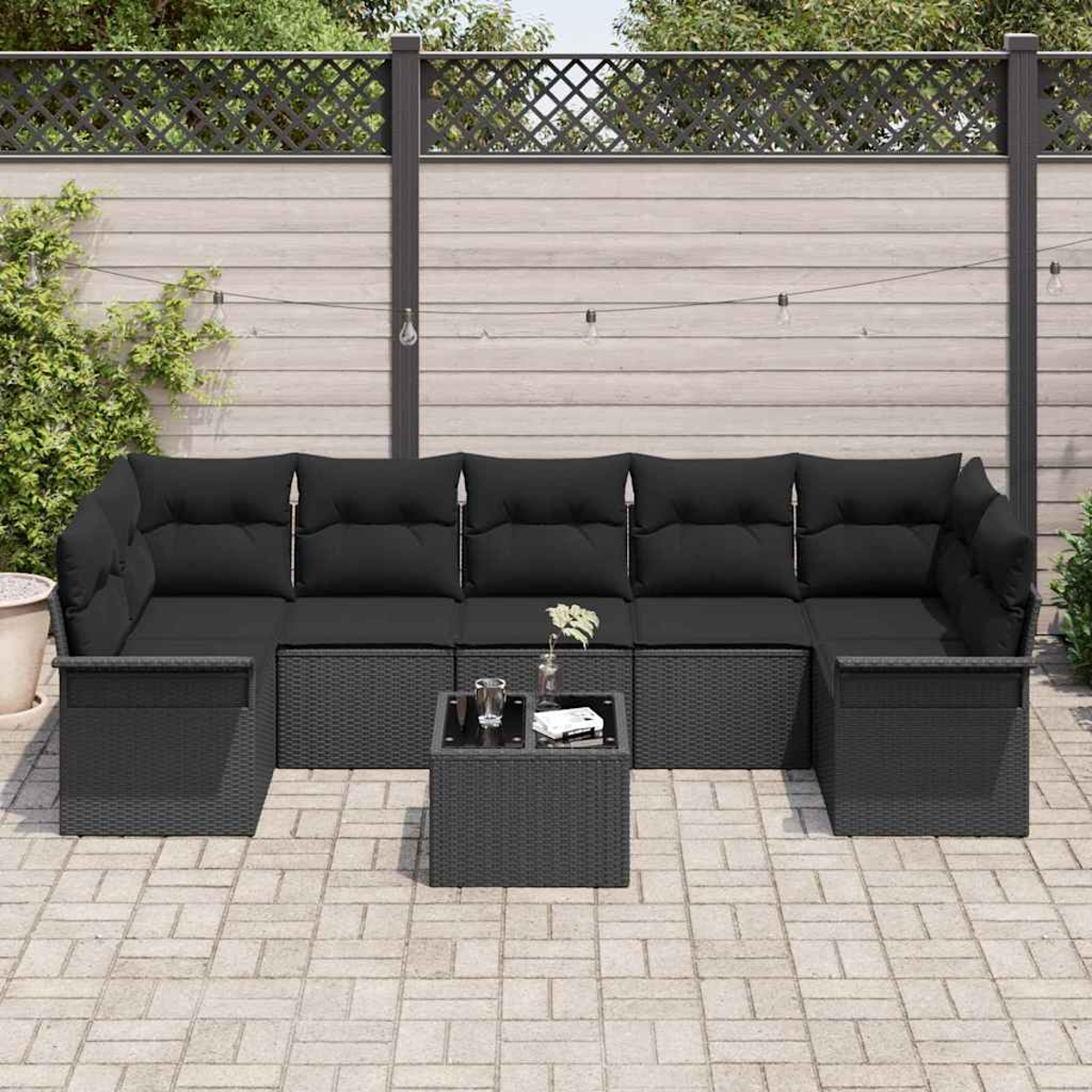 Schwarzes Ecksofa mit Kissen, kleiner Tisch mit Glas und Pflanzen. Auf einer Terrasse mit Holzzaun im Hintergrund.