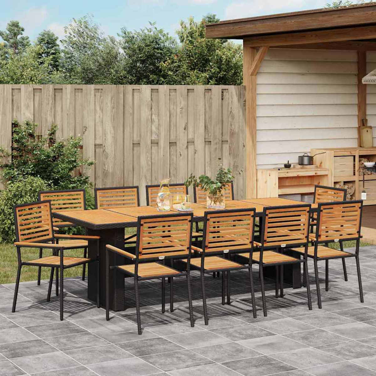 Ein Esszimmer-Set im Freien mit Holztisch und Stühlen steht auf einer Terrasse. Ein Holzzaun und eine kleine Holzkonstruktion im Hintergrund.