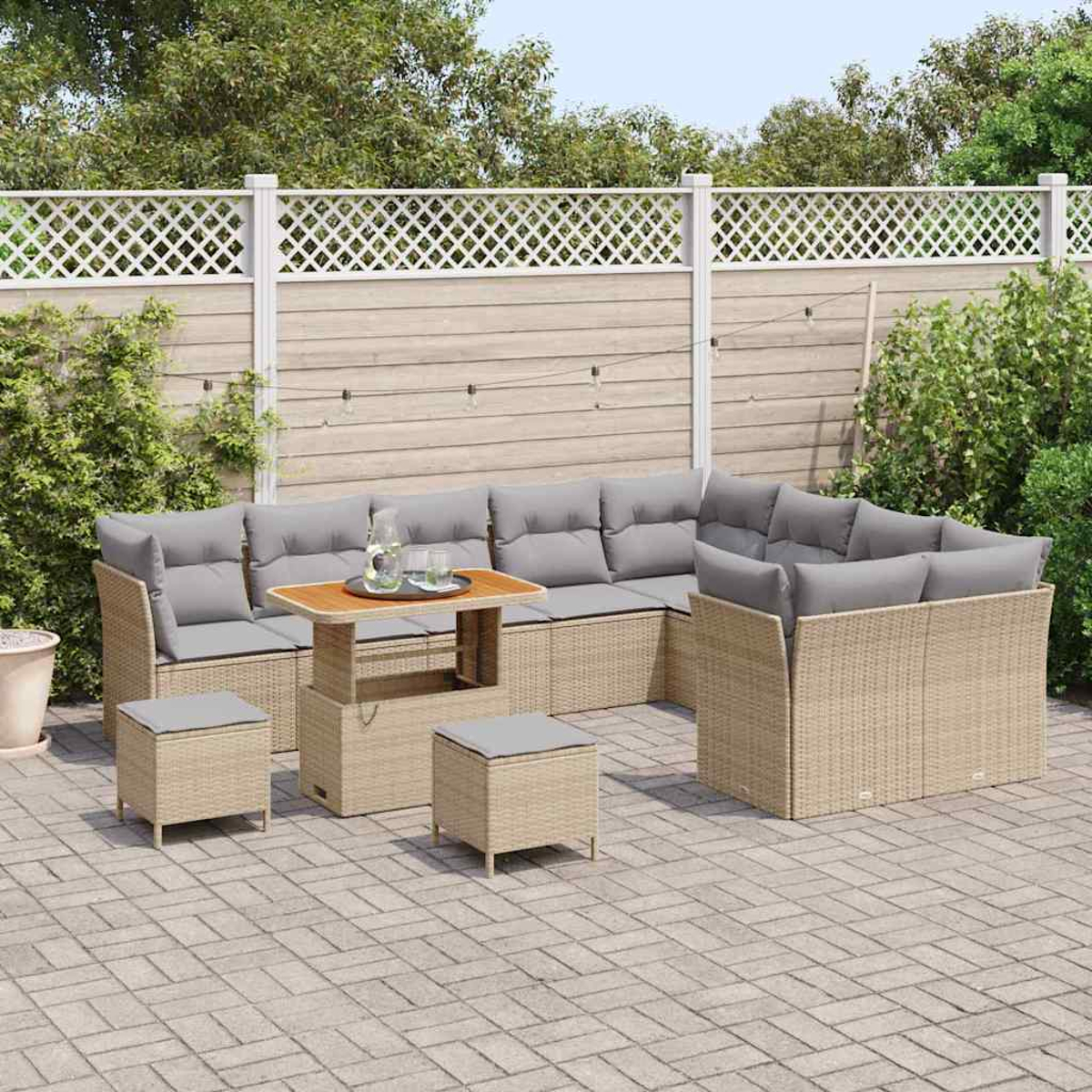 Garten-Terrassenset mit beigefarbenen gewebten Sofas, grauen Kissen, Holztisch und zwei Ottomanen auf einer Ziegelterrasse, mit Zaun im Hintergrund.