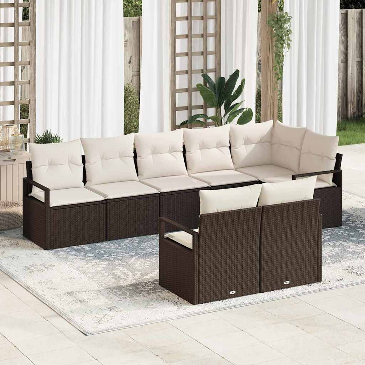 Outdoor-Ecksofa mit cremefarbenen Kissen. Dunkelbraunes Korbgeflecht. Weiße Vorhänge und ein Teppich. Pflanzen und eine Holzkonstruktion im Hintergrund.