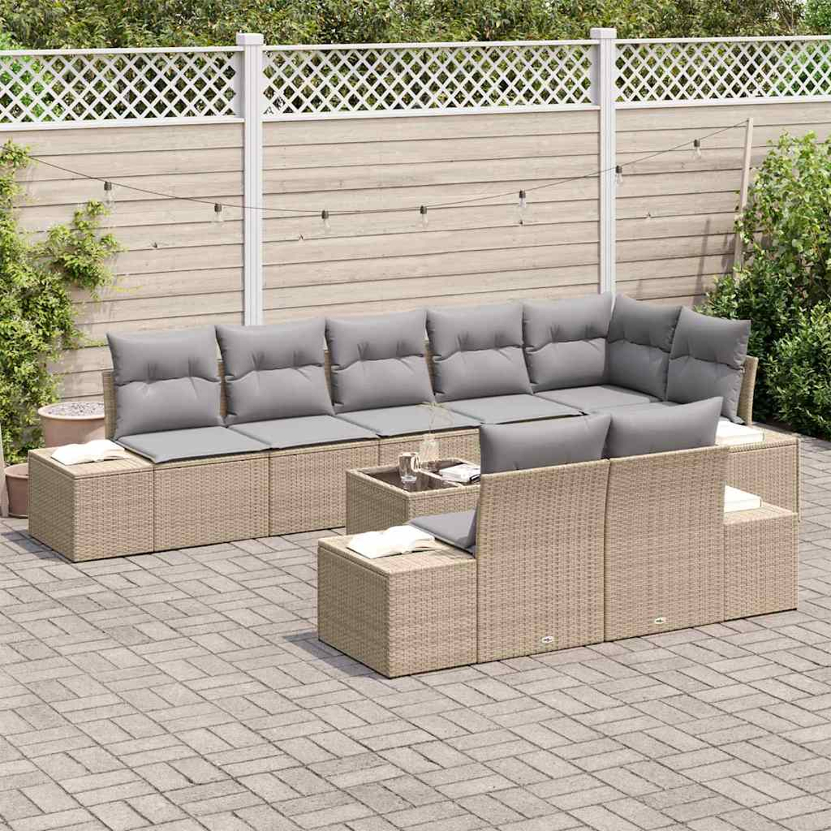 Outdoor-Sitzgruppe mit grauen Kissen, Korbmöbeln und einem kleinen Glastisch. Vor einem neutralen Zaun und gepflasterten Innenhof.