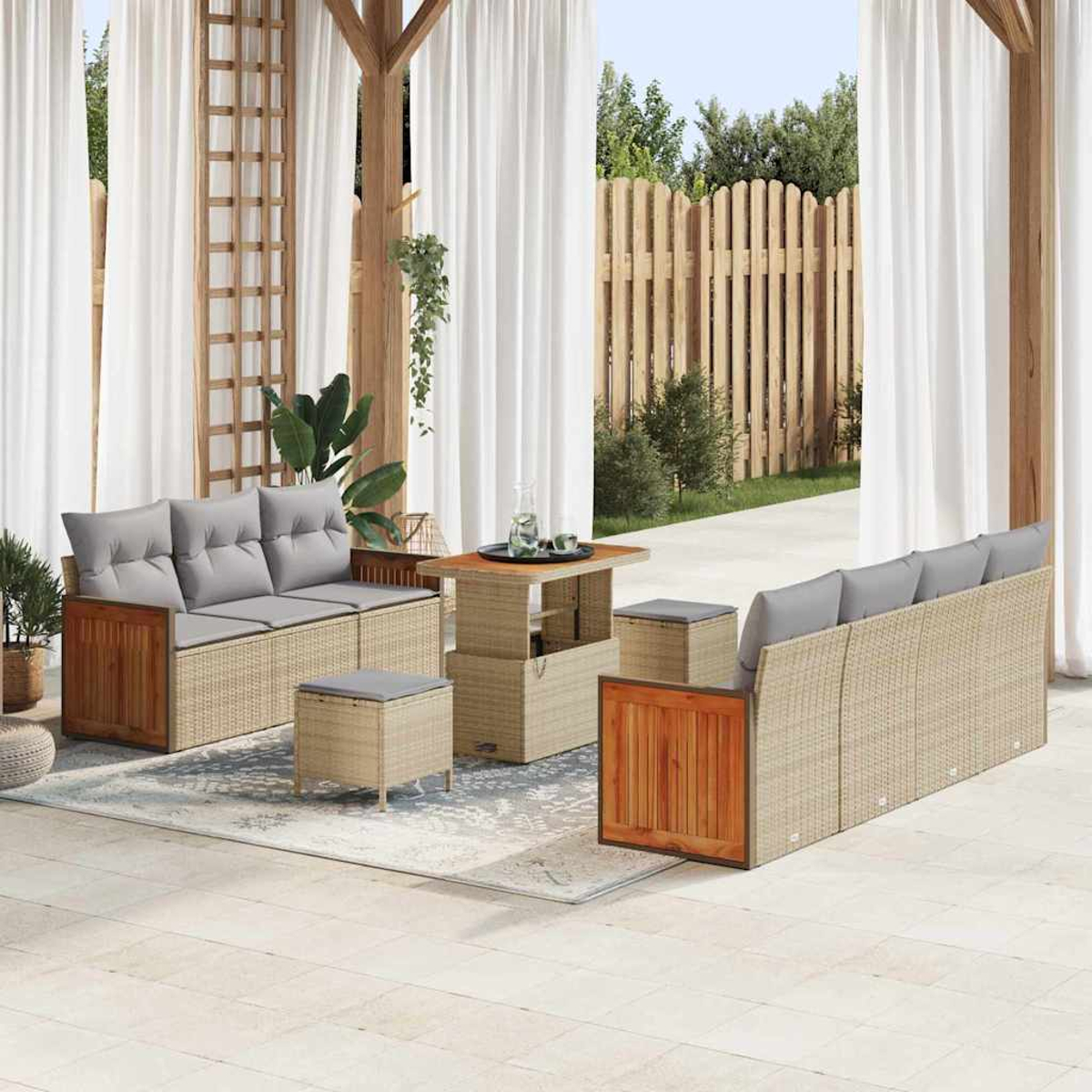 Outdoor-Sitzbereich mit Korbsitzmöbeln, Holztischen und weißen Vorhängen. Im Hintergrund ein Holzzaun und Grün.