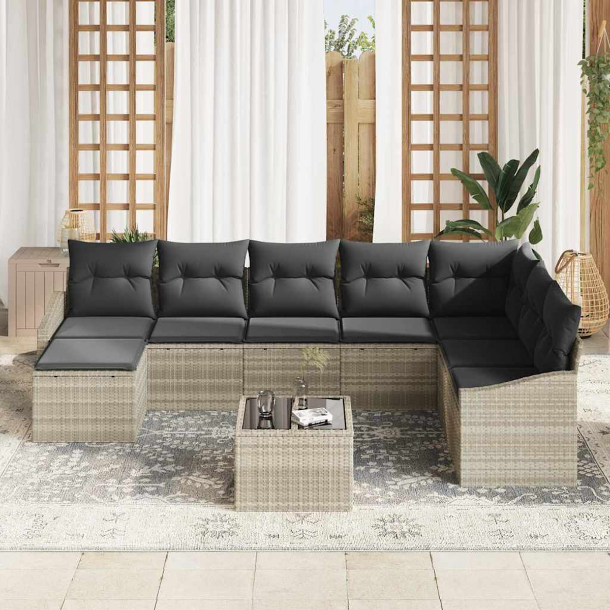 Sofá seccional exterior con cojines grises. Una mesita con tapa de cristal al frente. Cortinas y plantas al fondo.