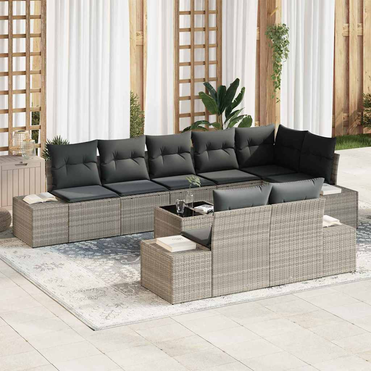 Sofá de ratán gris para exteriores con cojines negros. La escena incluye una alfombra, mesa de centro y plantas, con cortinas blancas.