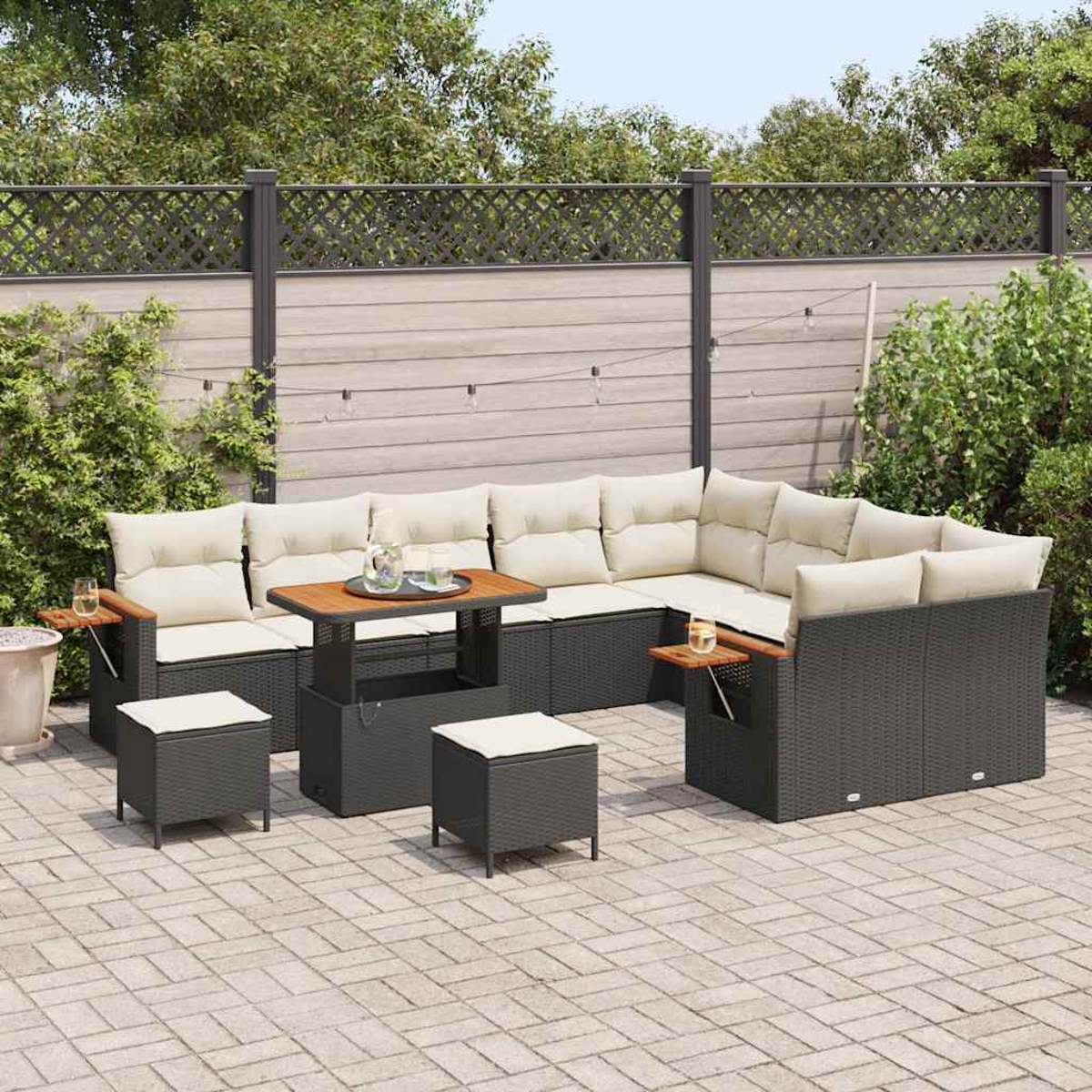 Outdoor-Sofa-Set mit beigefarbenen Kissen und einem Holztisch. Zwei kleine Hocker stehen davor. Im Hintergrund ein Zaun und Grün.