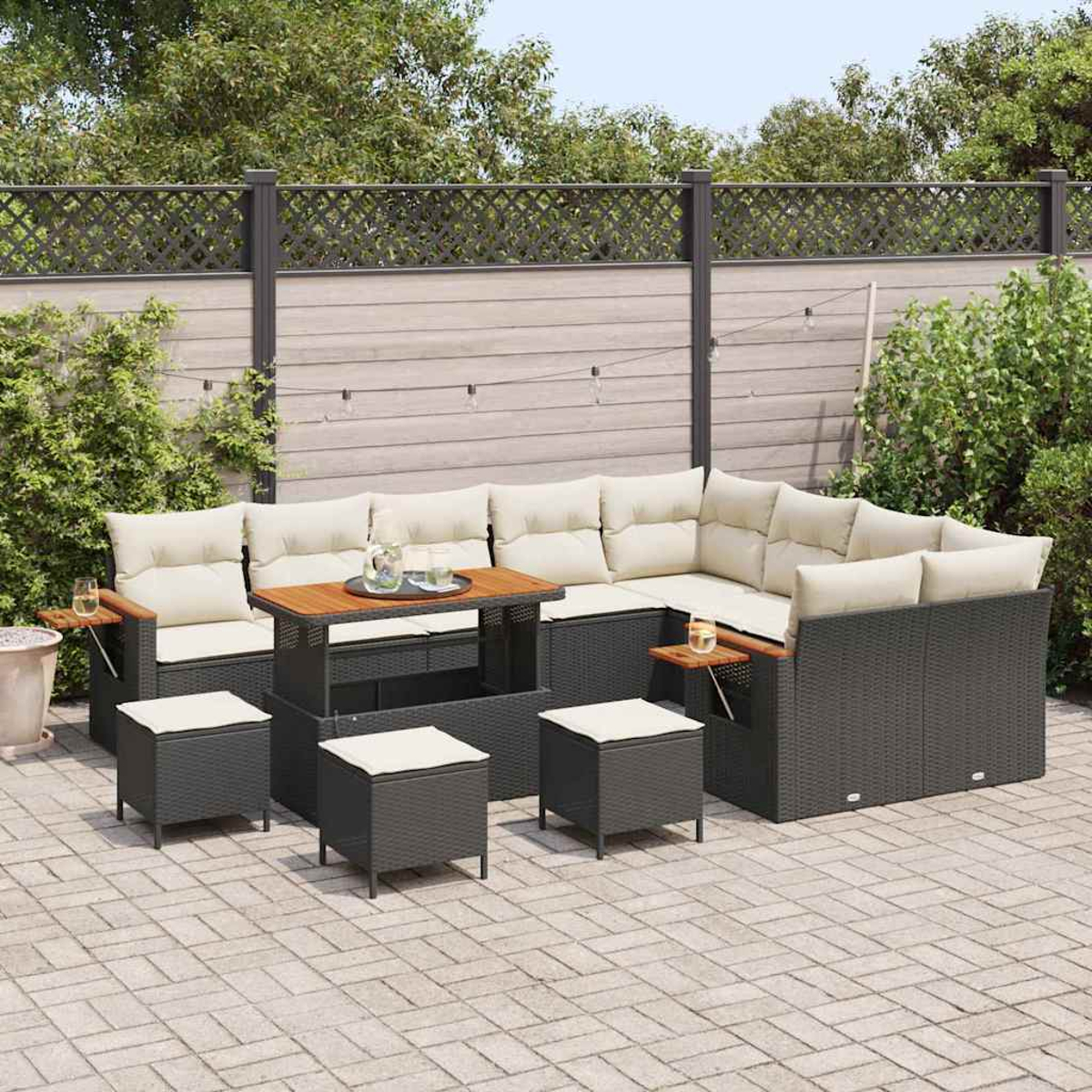 Gartenmöbel-Set auf einer Terrasse. Enthält ein Ecksofa mit beigen Kissen, einen Tisch und Hocker. Im Hintergrund ein Zaun und Bäume.