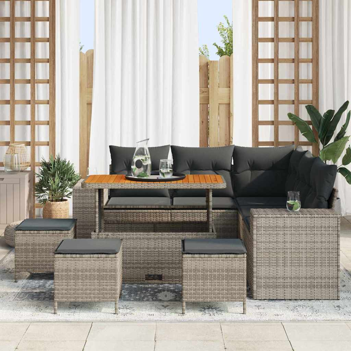 Set da patio esterno con cuscini grigi. Include tavolo, divano angolare e sgabelli. Lo sfondo presenta una recinzione e tende.