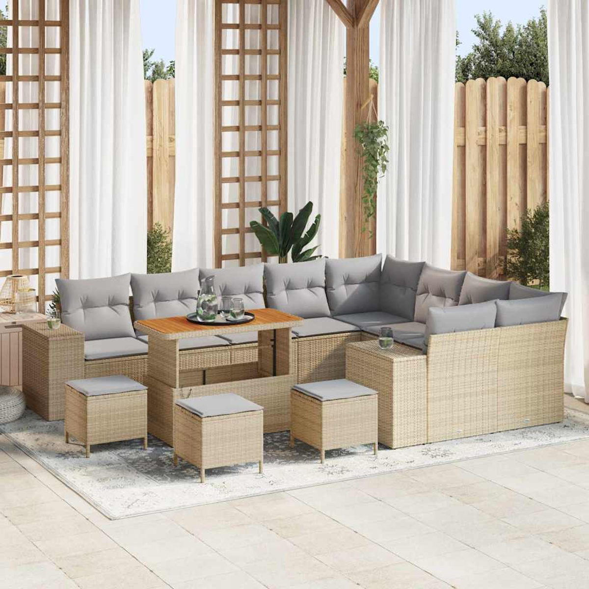 Divano componibile da esterno con cuscini grigi e tavolo in legno. Tende e staccionata in legno sullo sfondo. Visibili quattro pouf.