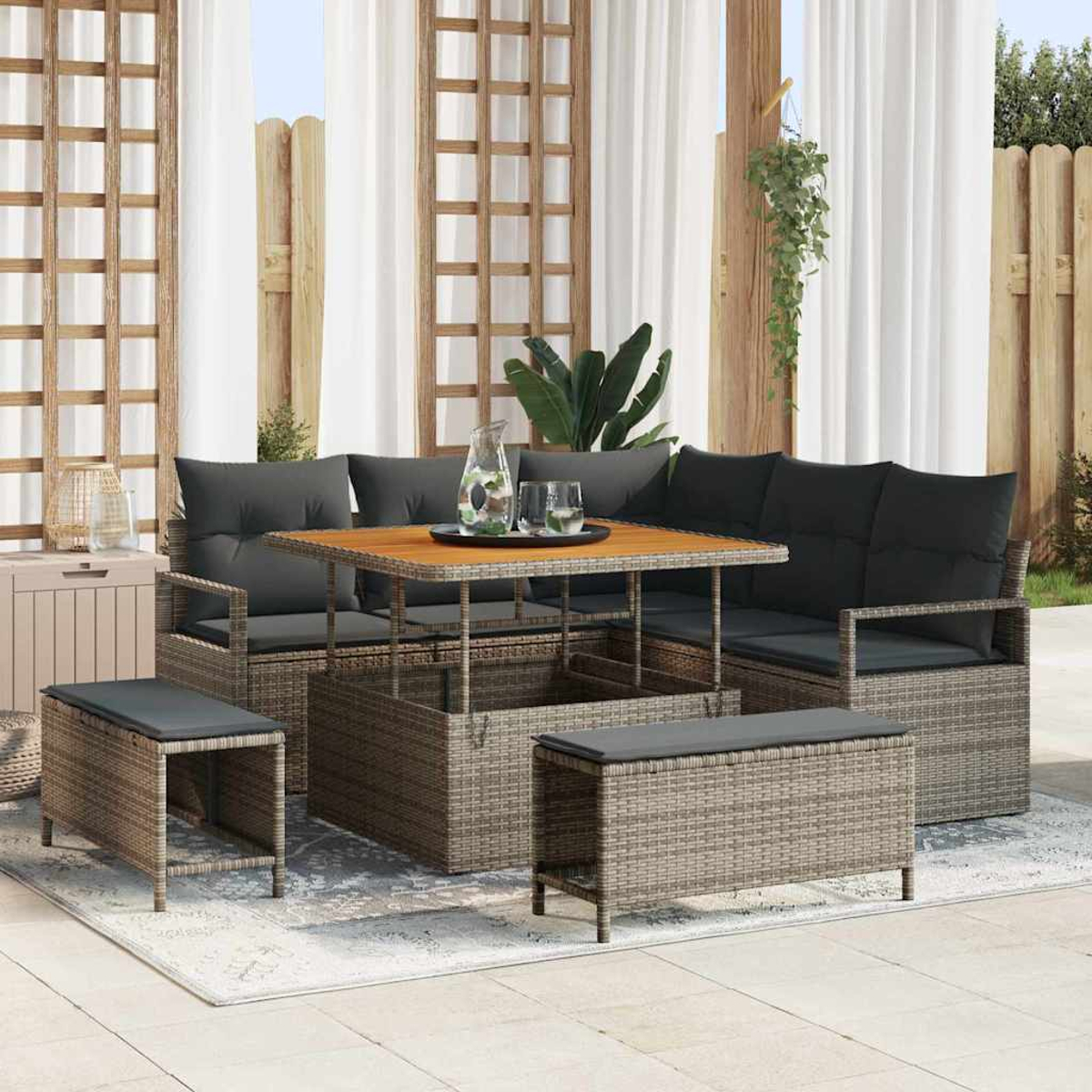 Juego de patio: sofá, mesa y bancos de ratán. Incluye cojines grises, tablero de madera y cortinas blancas al fondo.