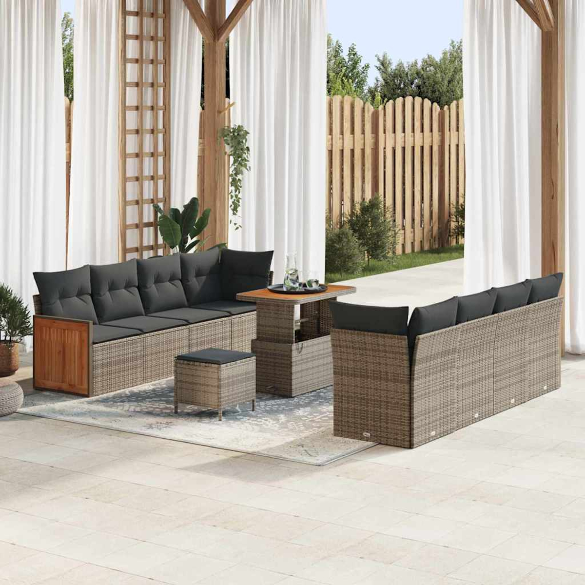 Gartenmöbel-Set: graue Kissen auf Korbsesseln, kleiner Tisch und Hocker auf einer Terrasse, mit weißen Vorhängen und Holzzaun.