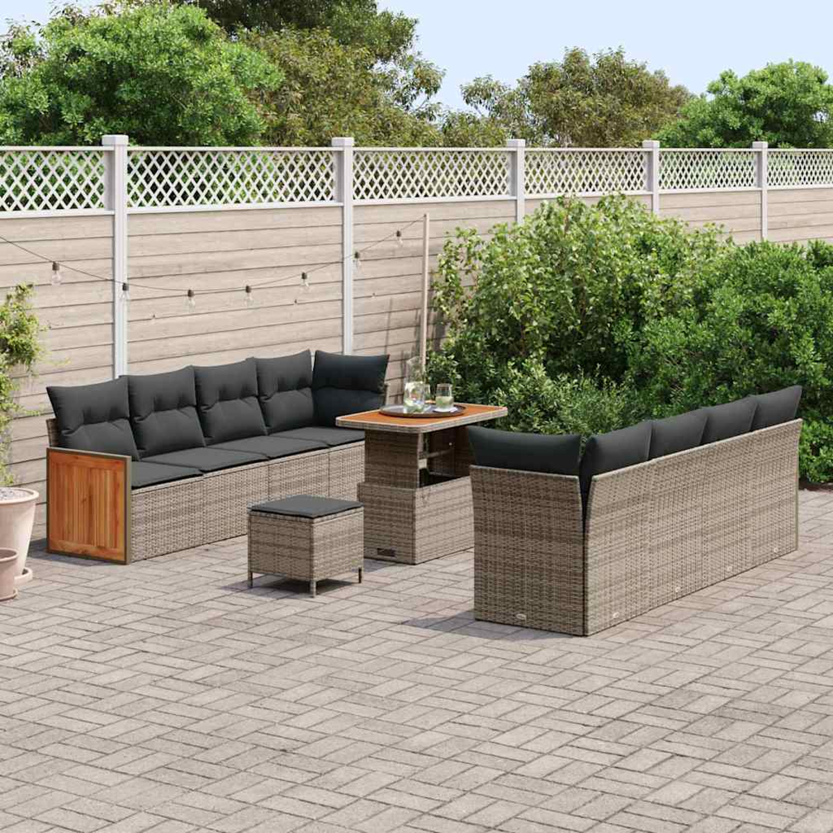 Gartenmöbel-Set. Sofa mit schwarzen Kissen, Tisch, Hocker und zweites Sofa. Auf Ziegelpflasterung.