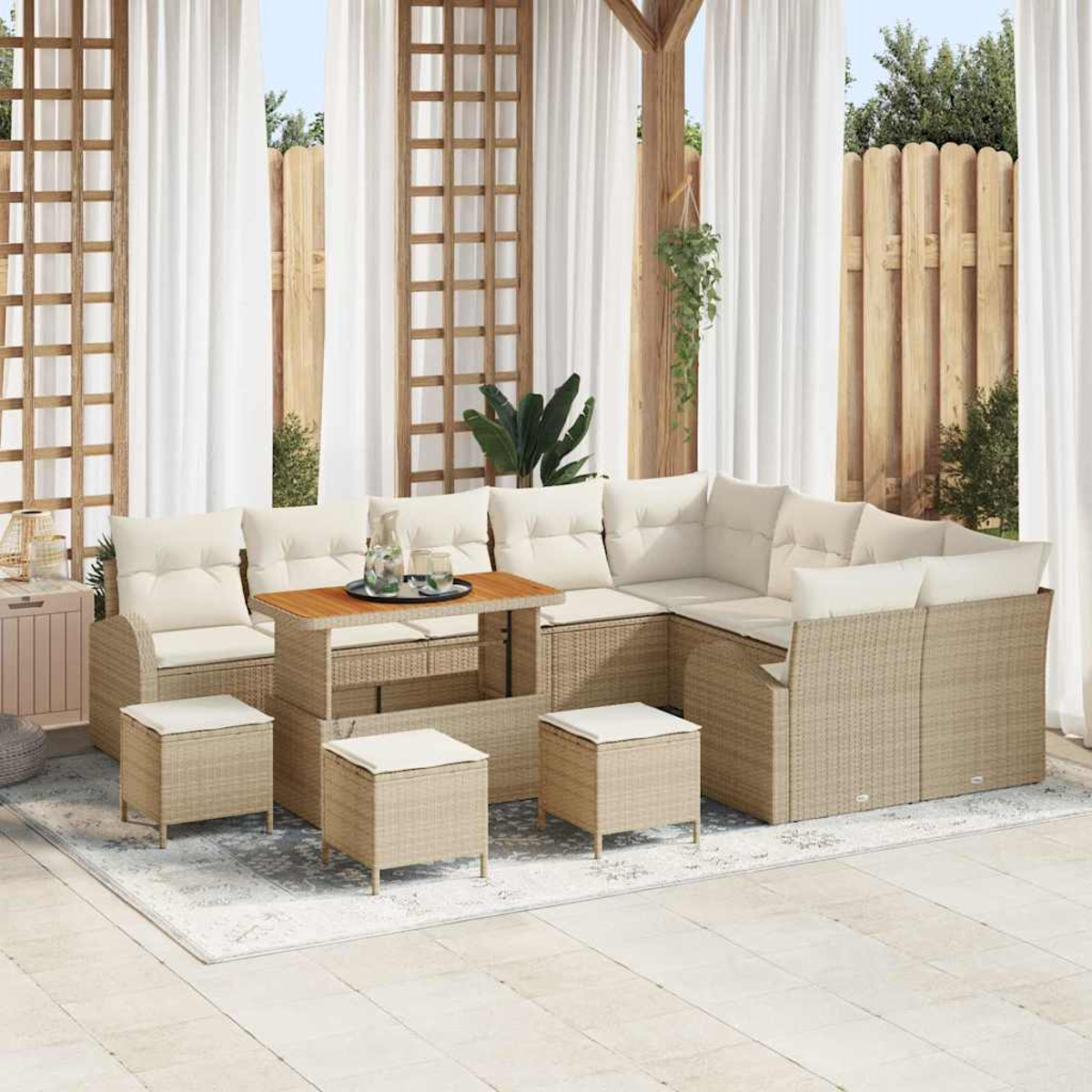 Garten-Terrassenset mit Ecksofa, Hockern und Couchtisch. Weiße Kissen, hellbraunes Korbgeflecht und neutrales Farbschema. Transparente Vorhänge im Hintergrund.