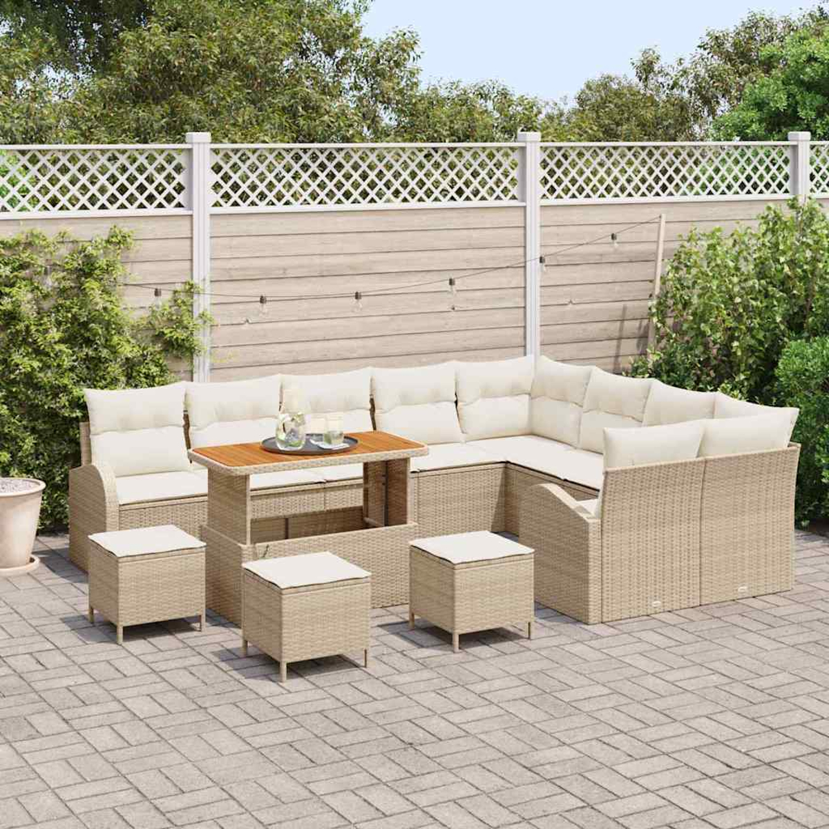Outdoor-Rattan-Möbelset: Ecksofa, Tisch und Hocker. Beige Kissen, Tischplatte aus Holz, alles auf einer gepflasterten Terrasse mit Zaun.
