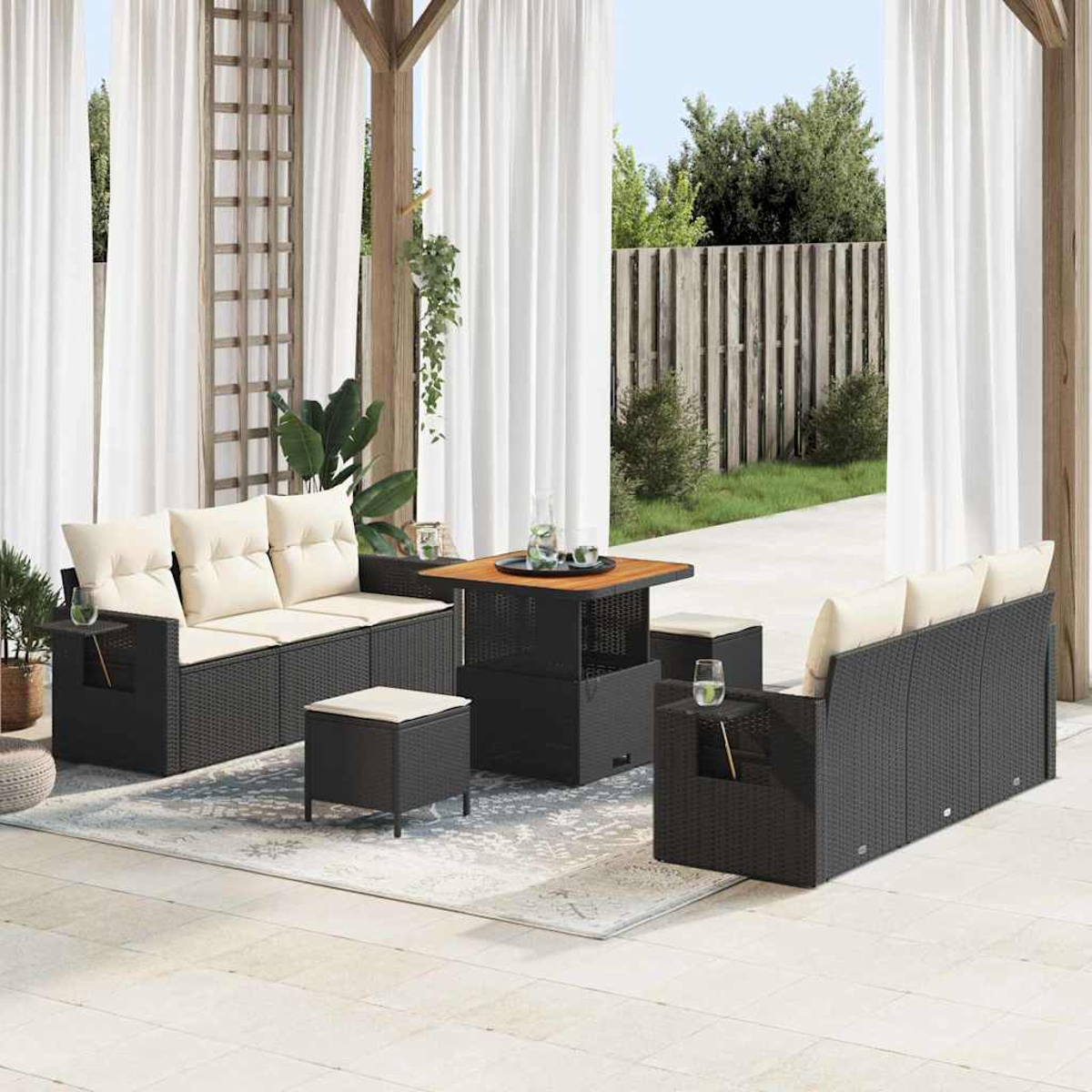 Garten-Terrassenset mit schwarzen Korbmöbeln, beigen Kissen, einem Tisch und Vorhängen. Inklusive Teppich und Holzzaun im Hintergrund.