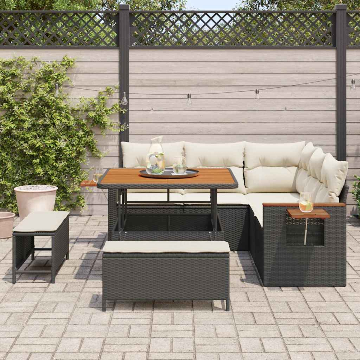 Gartenmöbel-Set aus Korbgeflecht mit Tisch, Bänken und Kissen. Krug, Gläser und ein Tablett stehen auf dem Tisch. Holzzaun im Hintergrund.