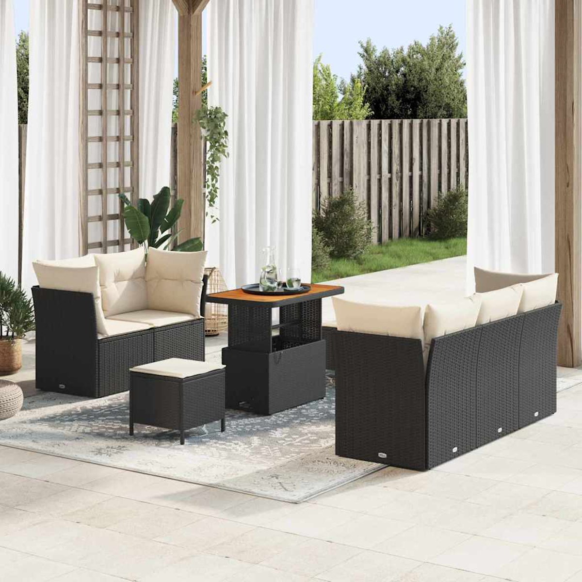 Outdoor-Sitzgruppe mit schwarzen Korbmöbeln, beigen Kissen und einem Tisch mit Holzplatte. Weiße Vorhänge und ein Holzzaun sind im Hintergrund.