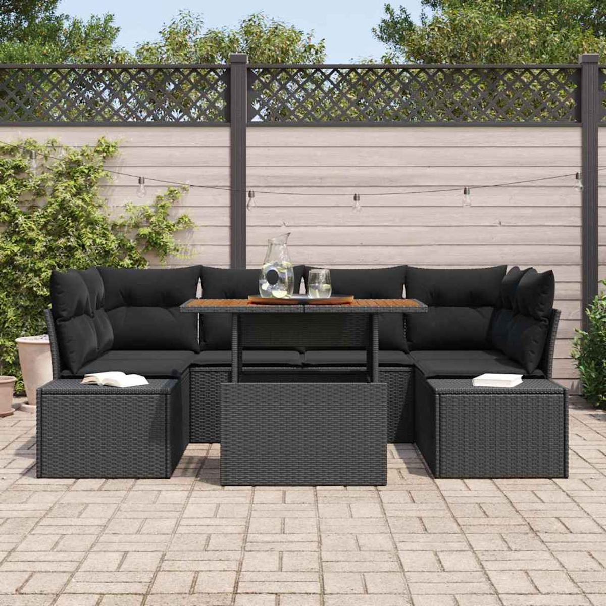Schwarzes Outdoor-Sofa mit Kissen, Couchtisch und Ottomanen. Dahinter ein Holzzaun und Lichterketten.