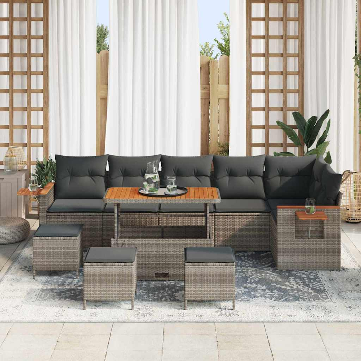 Set da patio in vimini con cuscini grigi, tavolo in legno e sgabelli su un tappeto decorato.