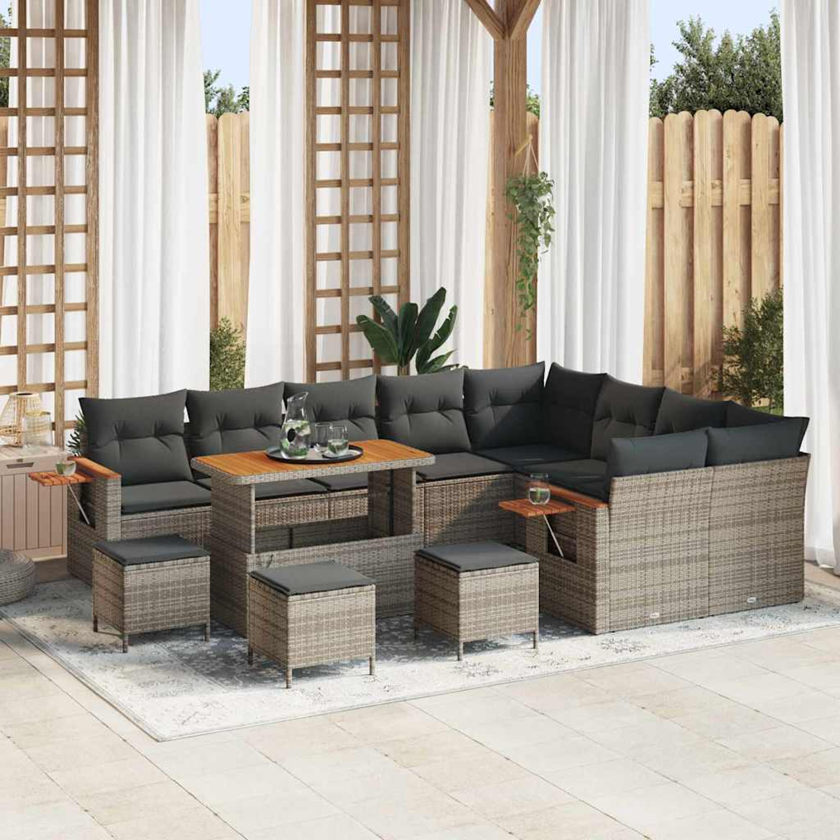 Outdoor-Ecksofa mit grauen Kissen, Holztisch und Hockern auf einem Teppich. Vorhänge und ein Holzzaun bilden den Hintergrund.