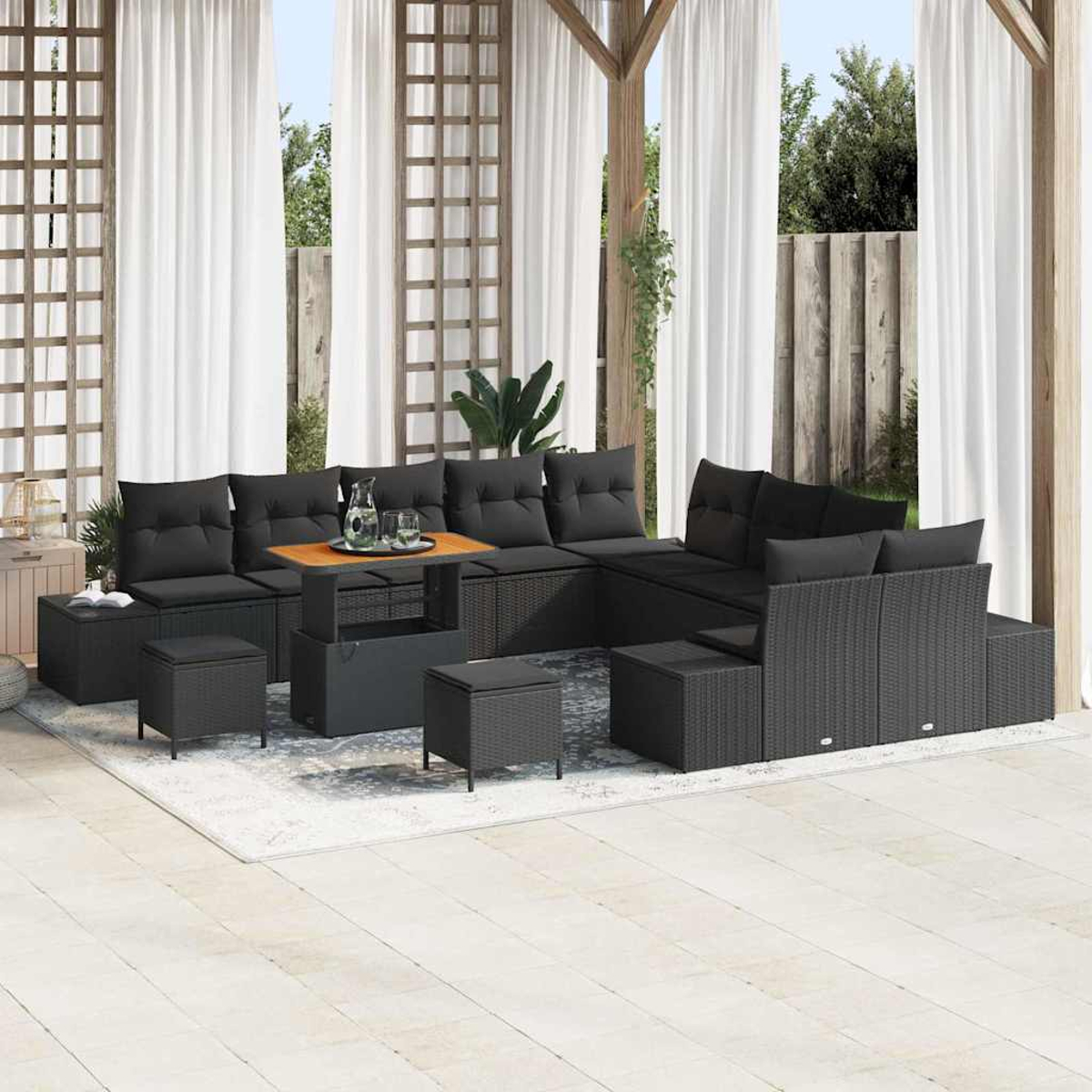 Ein schwarzes Outdoor-Ecksofa aus Korbgeflecht mit Kissen, Couchtisch und Hockern auf einem Teppich, unter einer Pergola mit weißen Vorhängen.