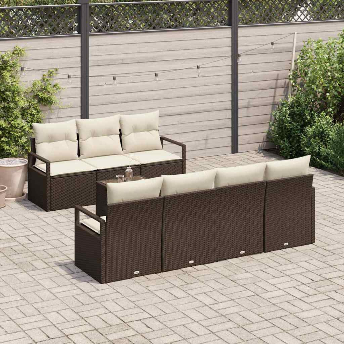 Juego de patio al aire libre con muebles de mimbre marrón, cojines beige y una pequeña mesa de vidrio. En un patio de ladrillos.