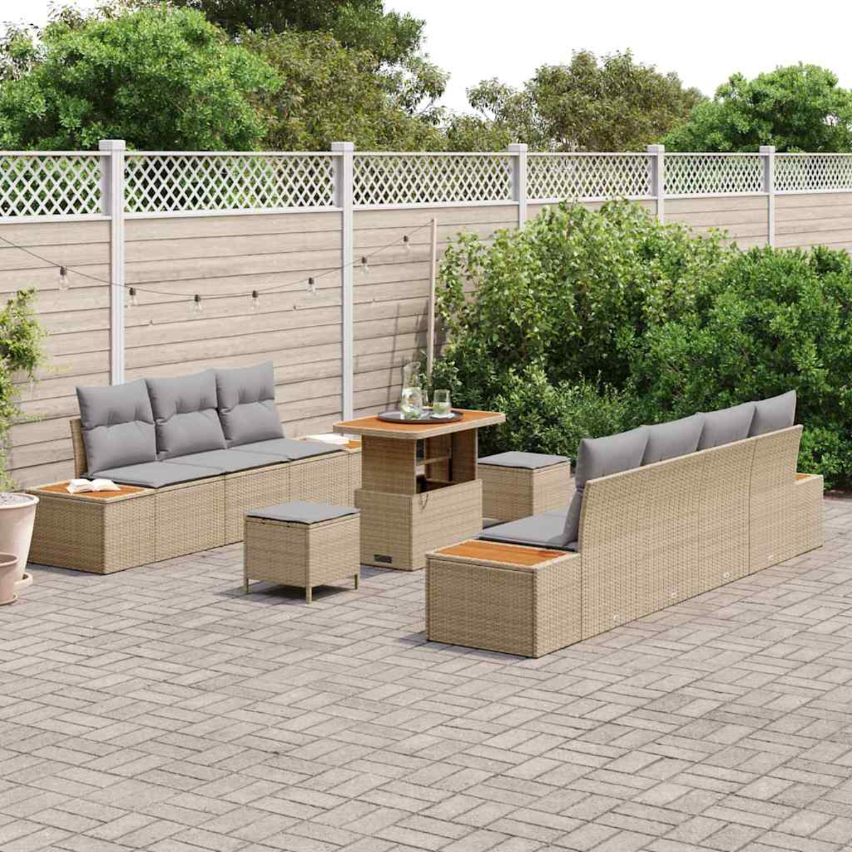 Garten-Terrassenset mit zwei Sofas, einem Tisch und Ottomanen. Graue Kissen, hellbraunes Korbgeflecht und Holztischplatten. Steingepflasterte Terrasse mit Zaun.