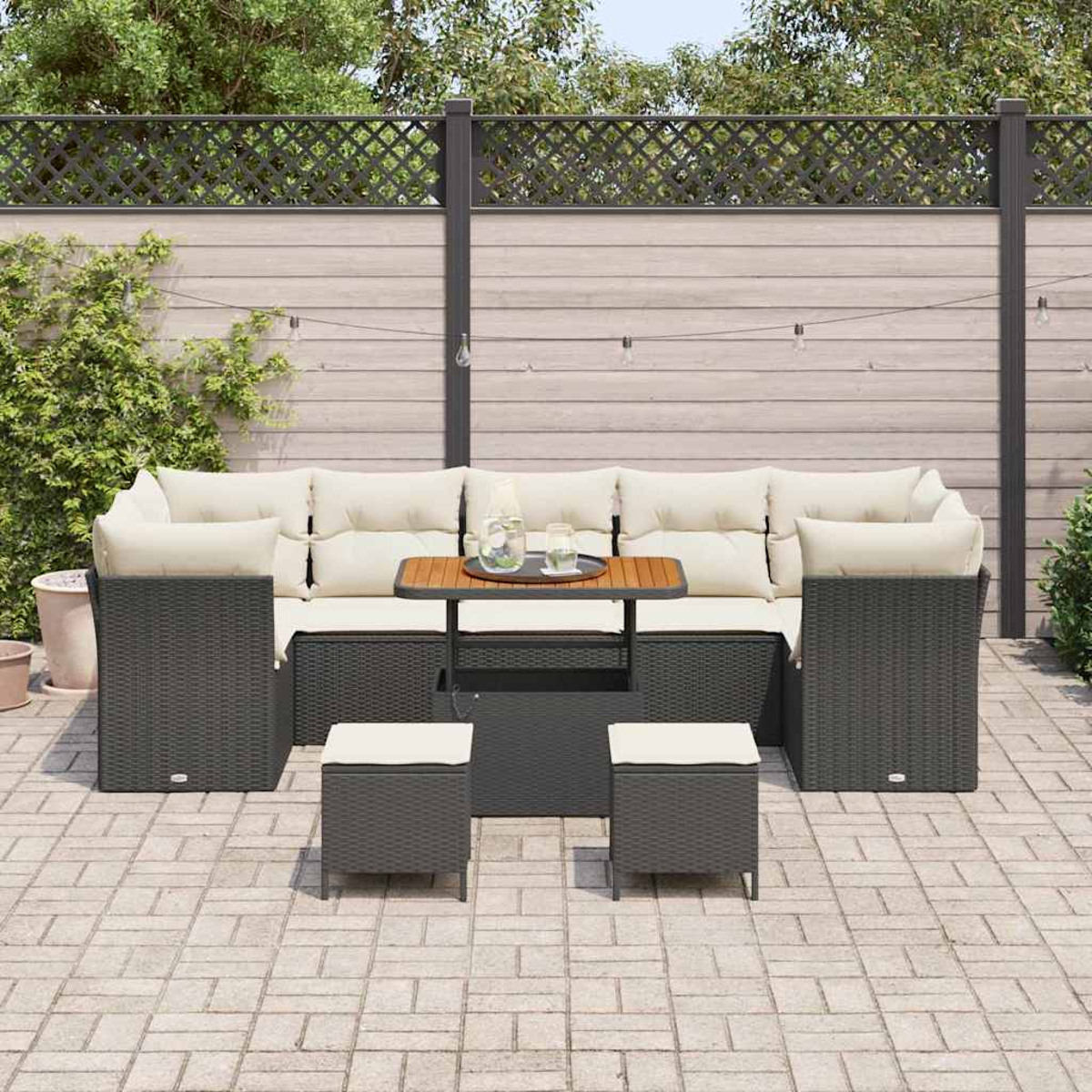 Set di mobili da esterno in vimini: divano, sedie, tavolino e pouf. Cuscini beige e tavolo in legno. Su patio in mattoni.