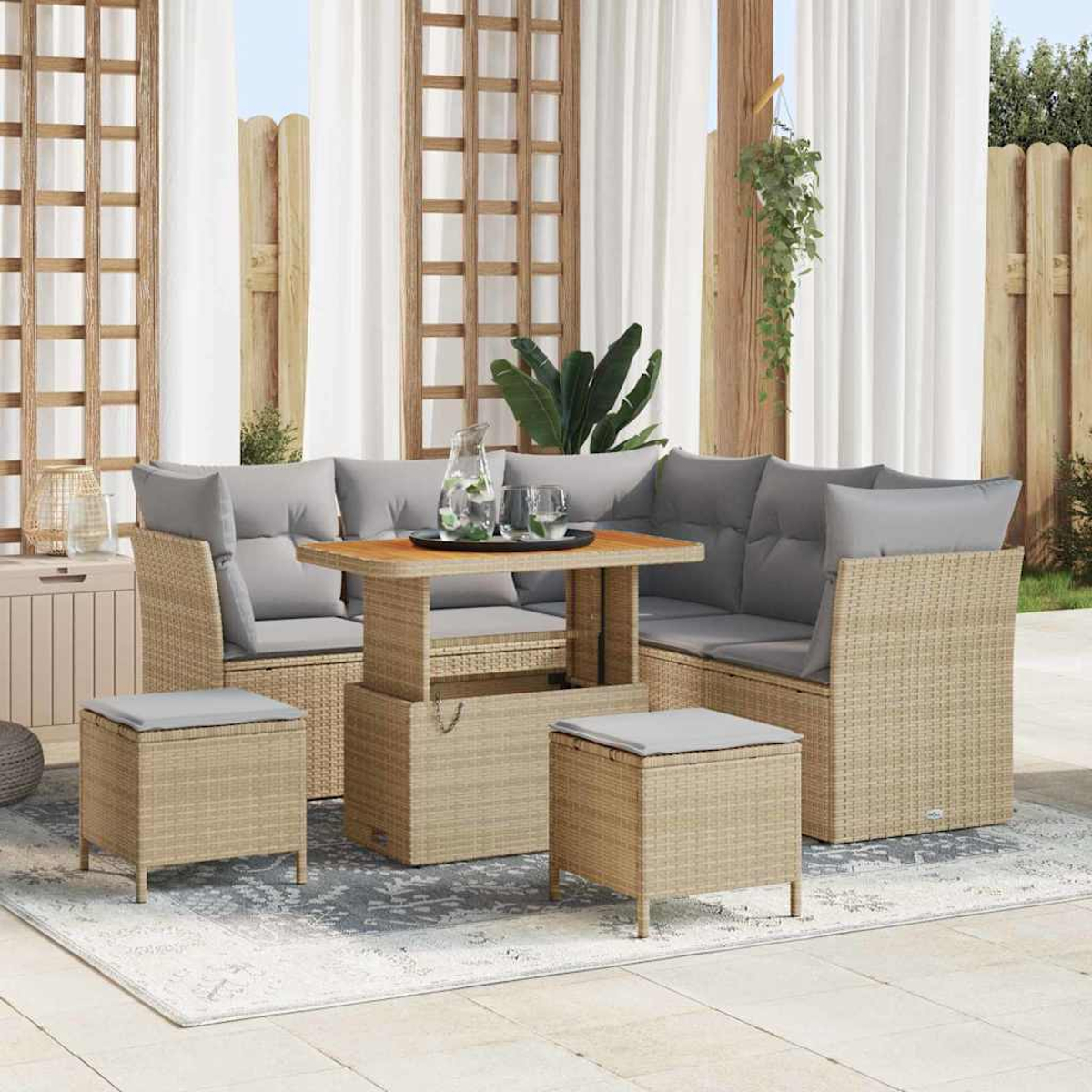 Outdoor-Rattan-Möbelset mit grauen Kissen, einem Tisch mit Getränken und zwei Ottomanen. Im Hintergrund Vorhänge und ein Holzzaun.