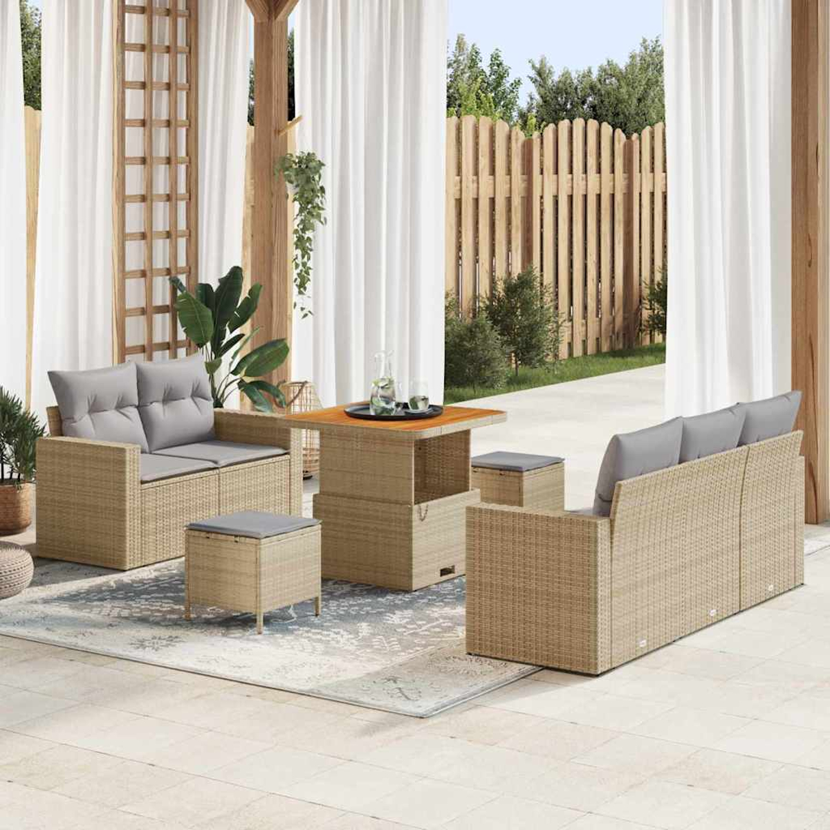 Set da patio esterno con divano, sedie, tavolo e pouf. Cuscini grigi su vimini beige. Tende bianche, recinzione in legno sullo sfondo.