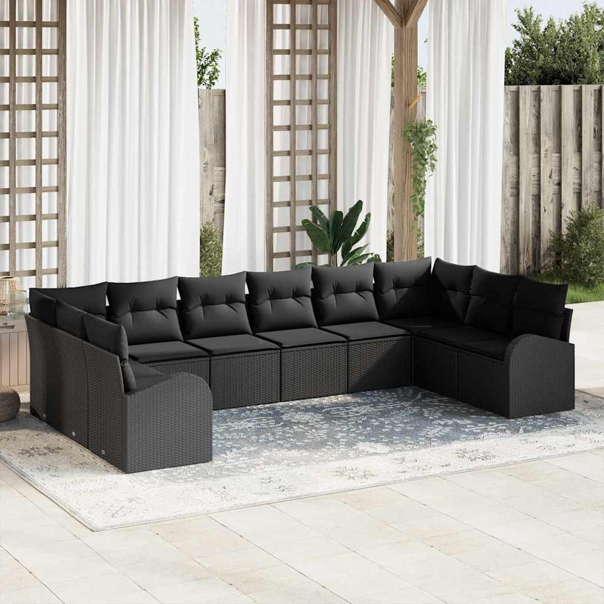 Ein schwarzes Korbsessel-Sofa mit Kissen steht auf einem gemusterten Teppich. Weiße Vorhänge und ein Holzgitter im Hintergrund.