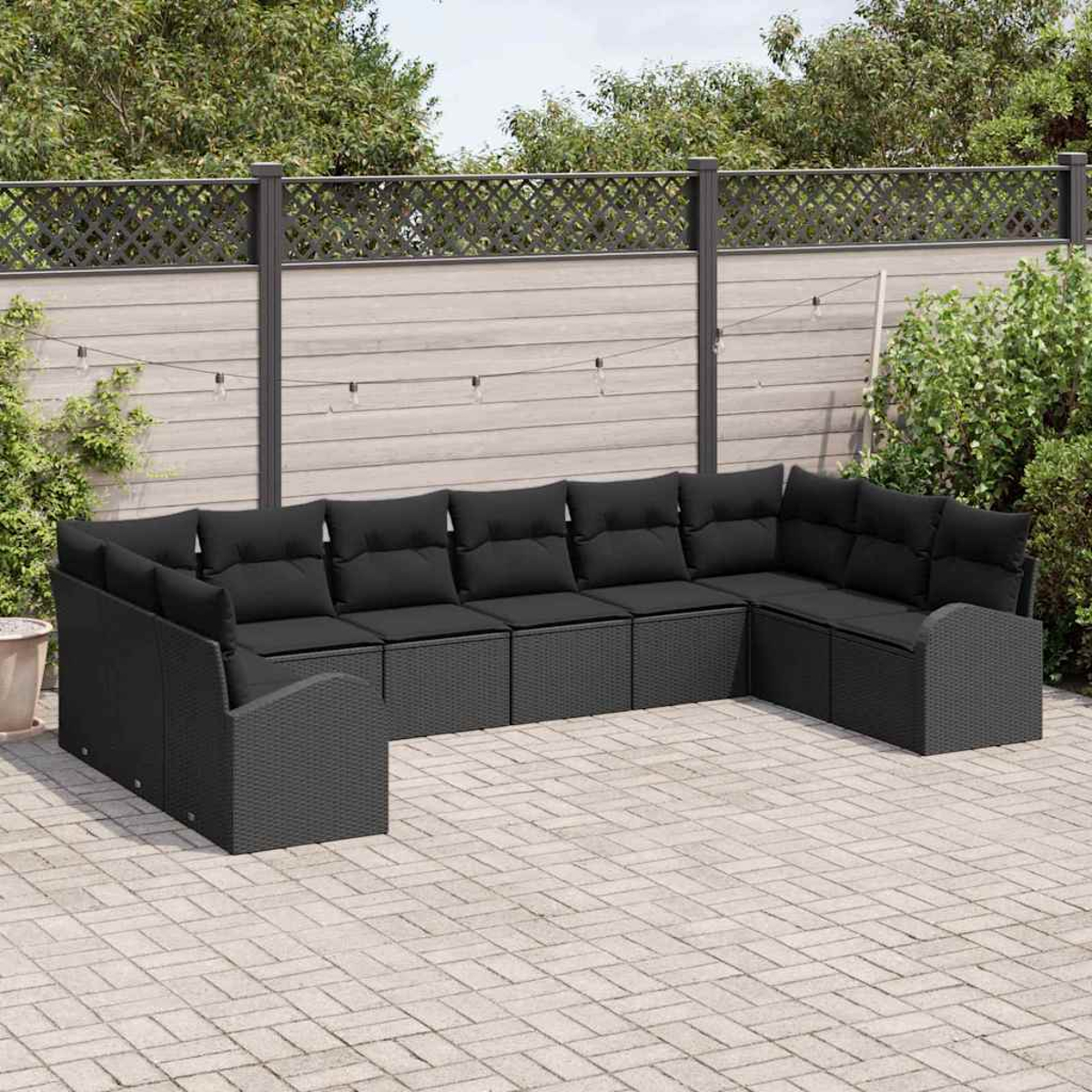 Schwarzes Outdoor-Ecksofa auf einer Terrasse. Das Sofa hat schwarze Kissen und ist L-förmig angeordnet. Im Hintergrund befinden sich ein Zaun und Pflanzen.